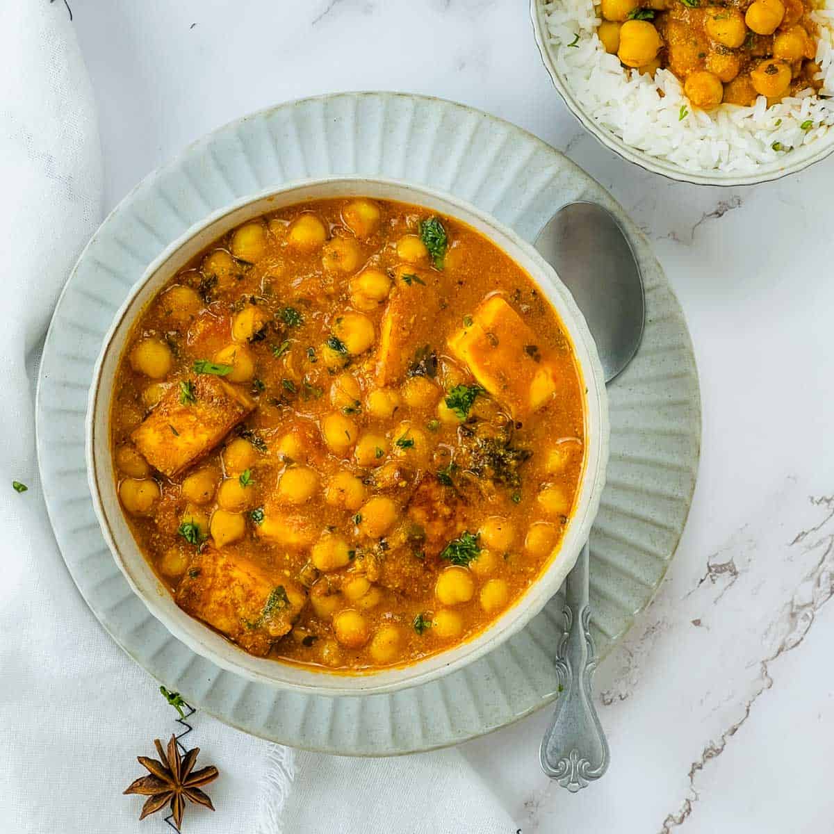 Chana paneer in a white bowl with another bowl of rice and chana paneer in the background.