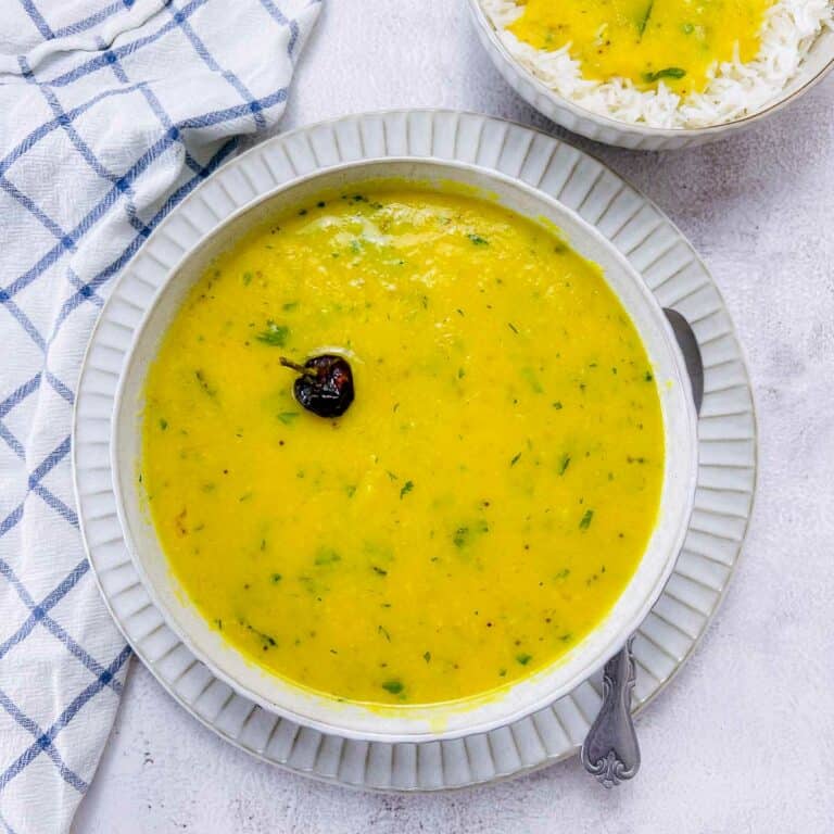 Yellow dal in a white bowl placed on a white surface.