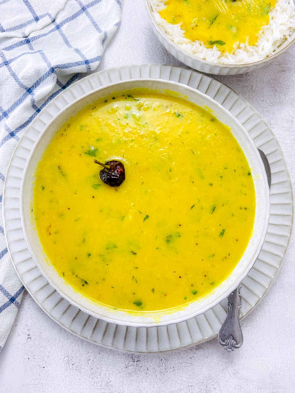 Home-style dal in a white bowl with rice and dal in another bowl.