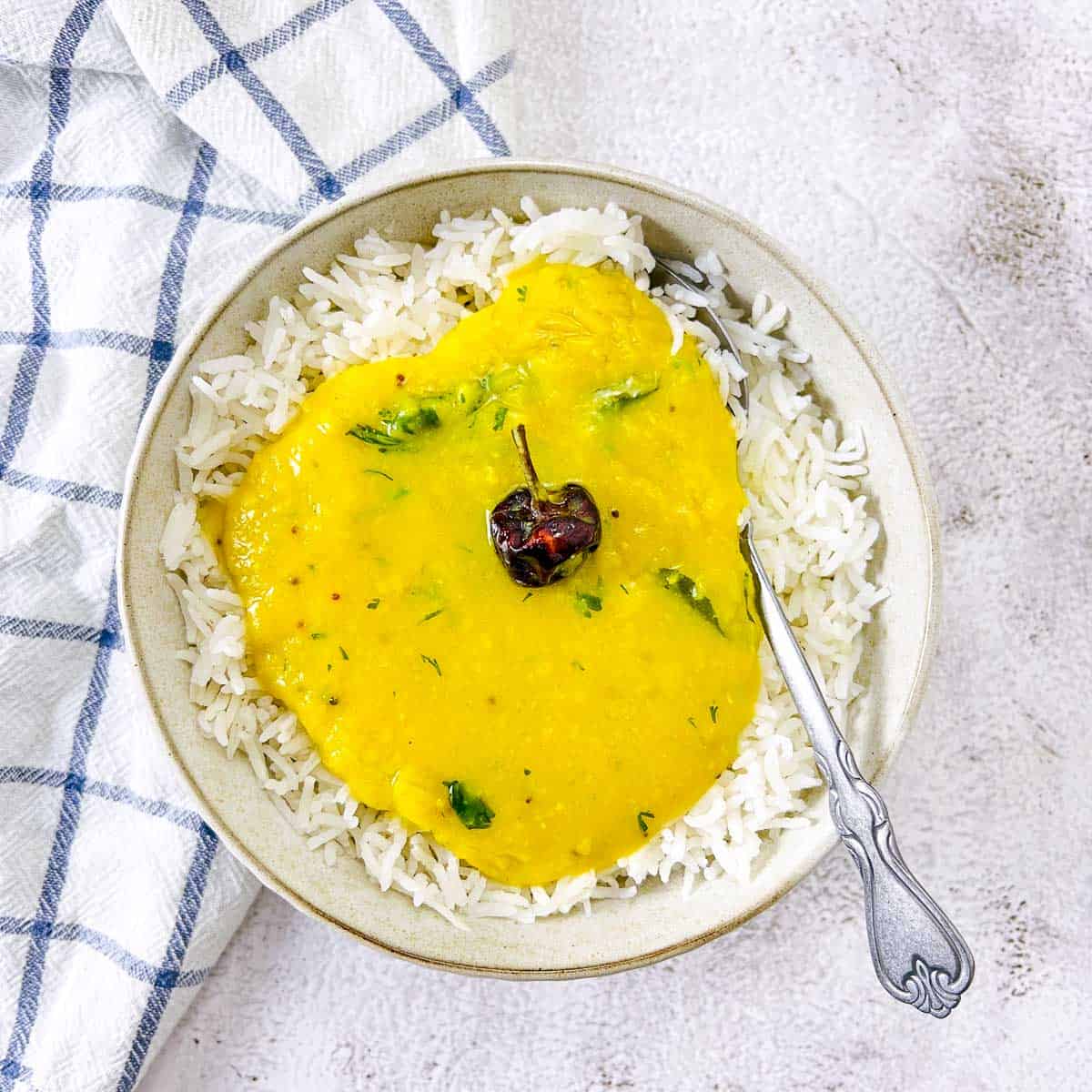 A bowl of rice topped with dal with a spoon placed in the bowl.