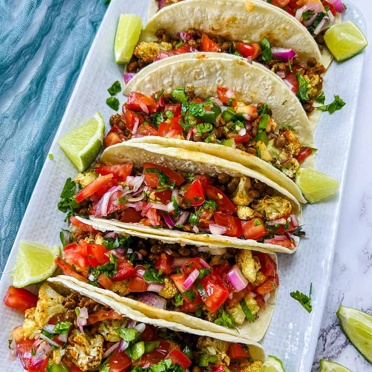 Cauliflower lentil tacos with pico de gallo on white surface.