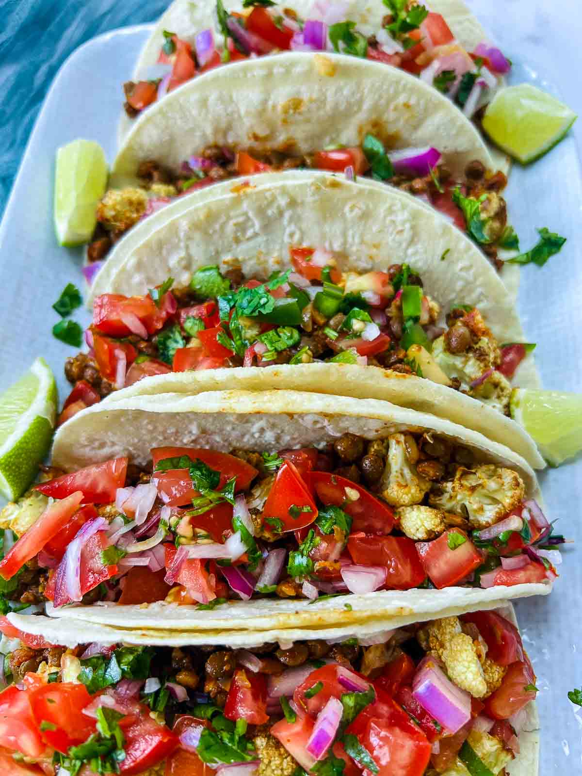 Cauliflower lentil tacos topped with cilantro and lime wedges.