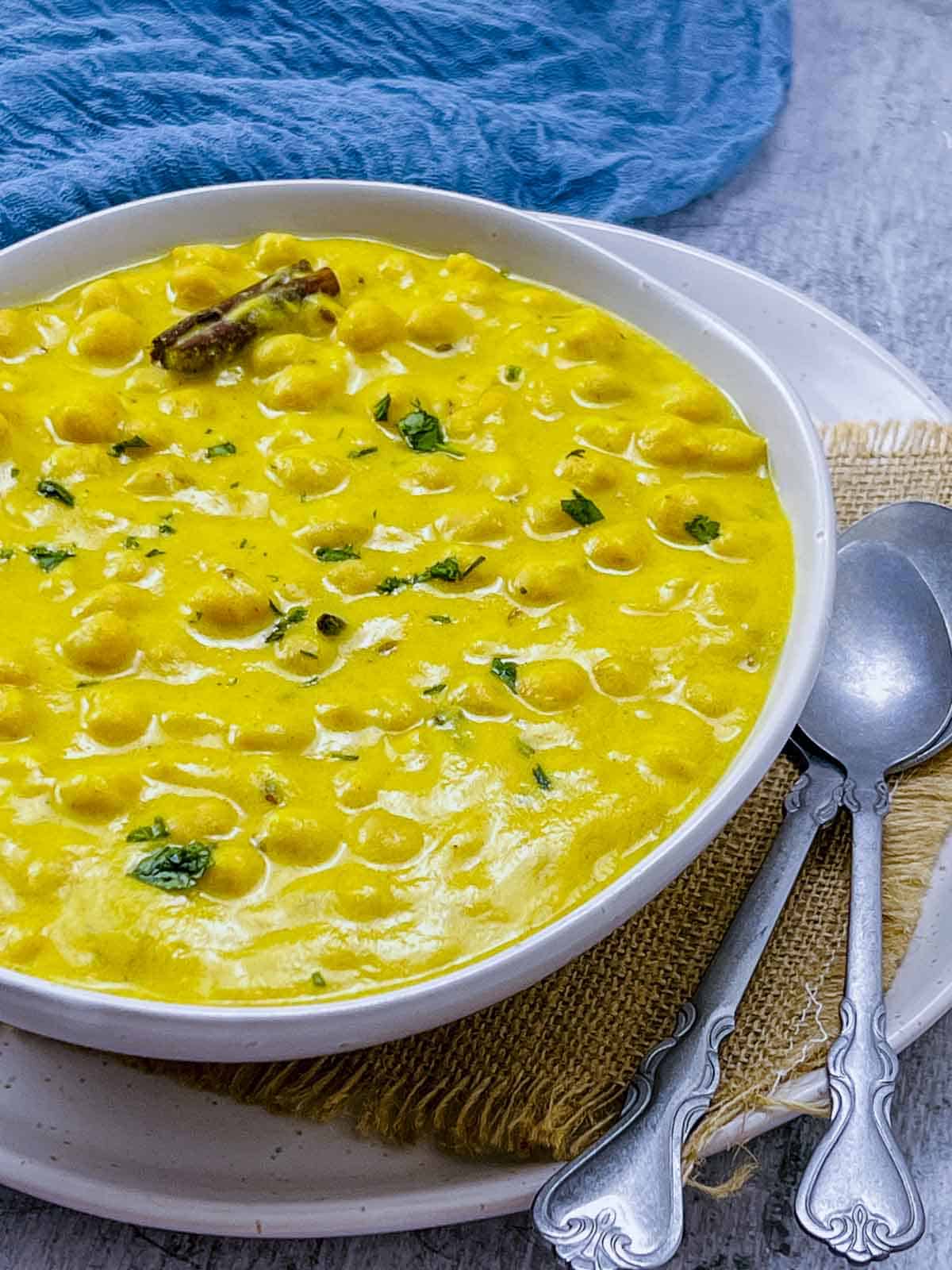 Chana madra garnished with cilantro in a white bowl with spoons in the background.