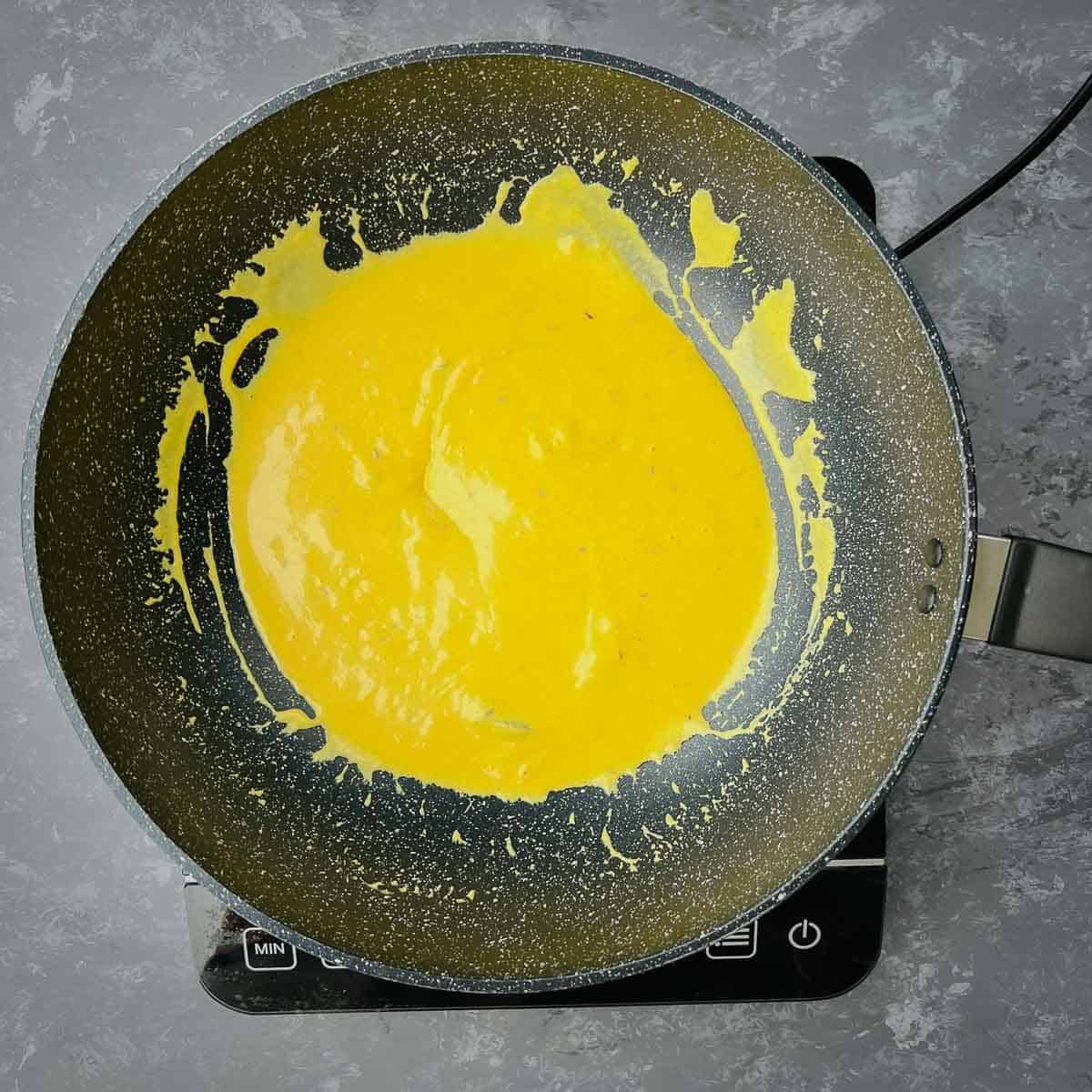 Yogurt mixture cooked with spices in frying pan.