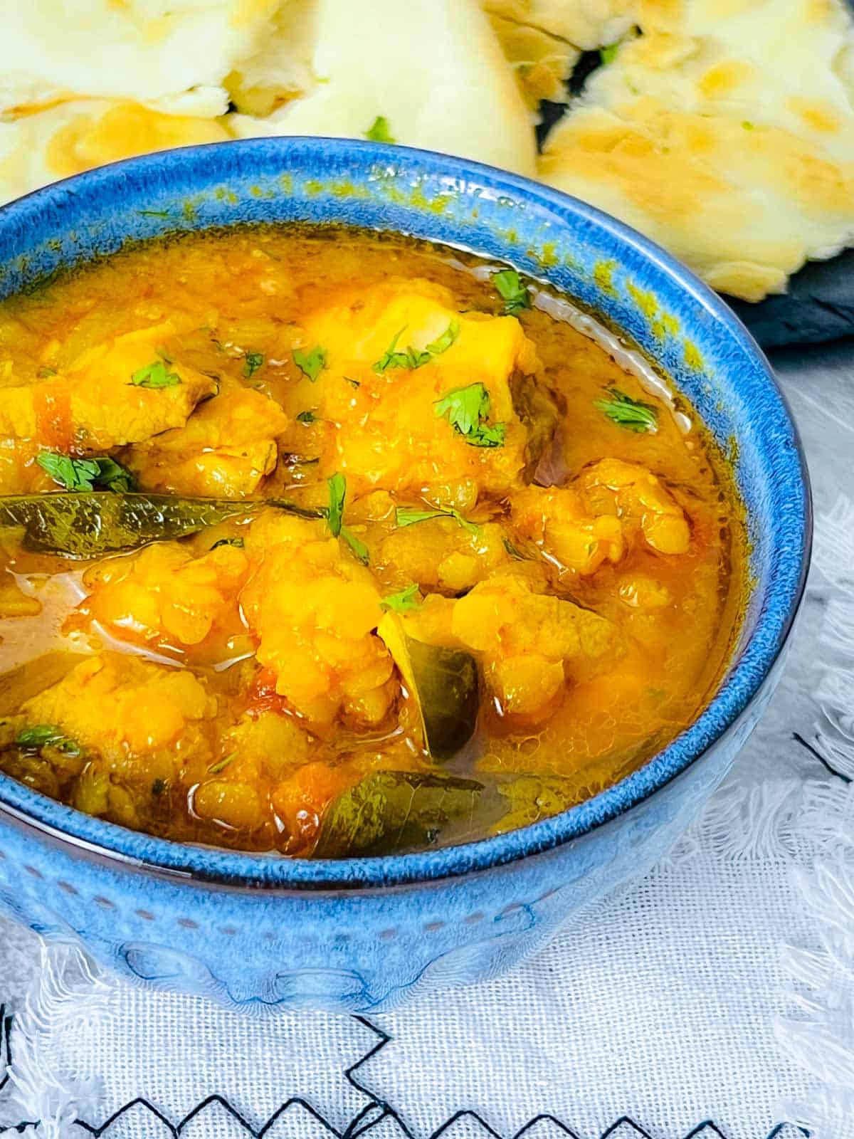Chicken red lentil curry or dal murgh in a blue bowl with naan in the background.