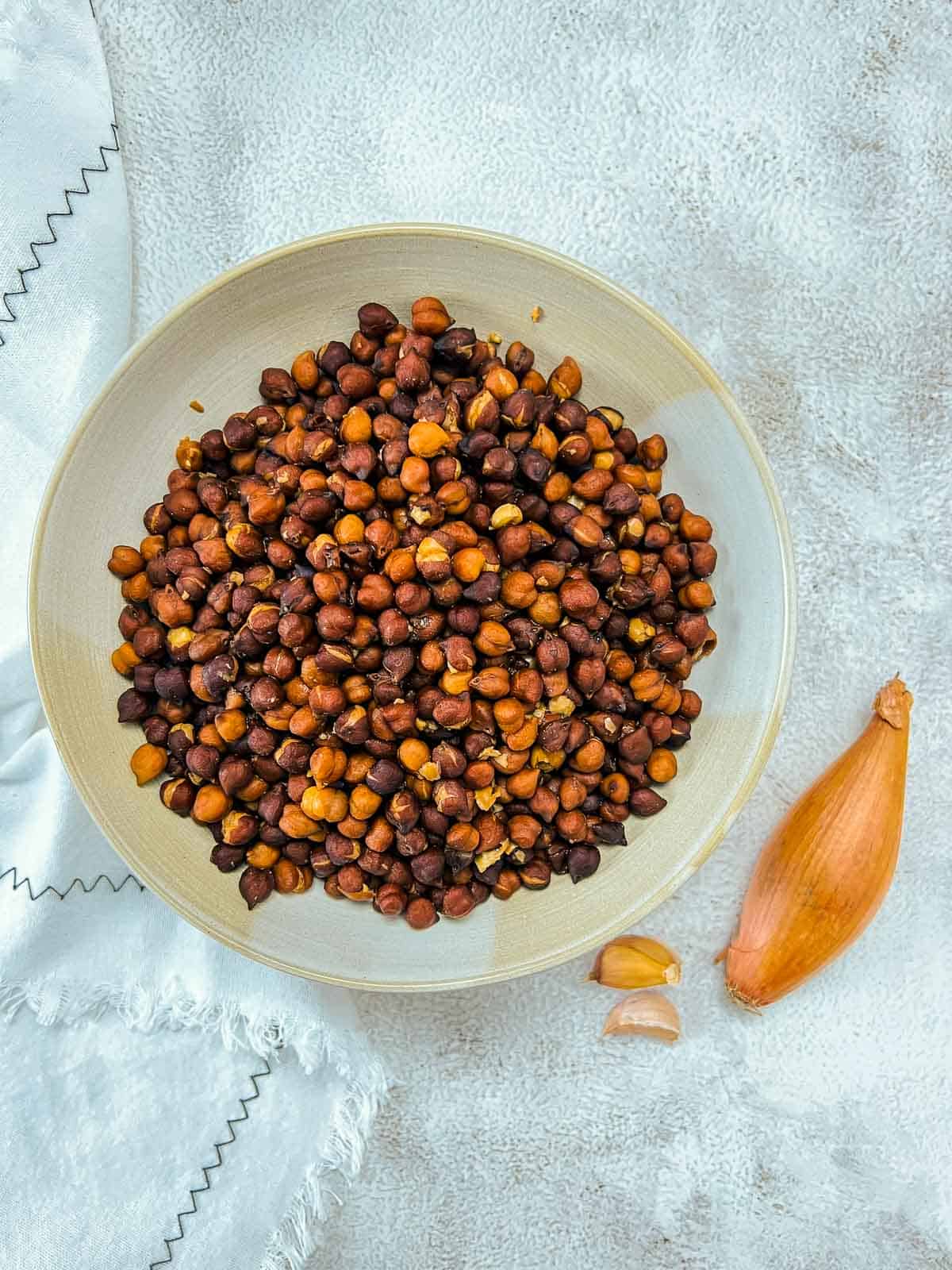 Cooked black chickpeas in a wide bowl with shallot in the background.