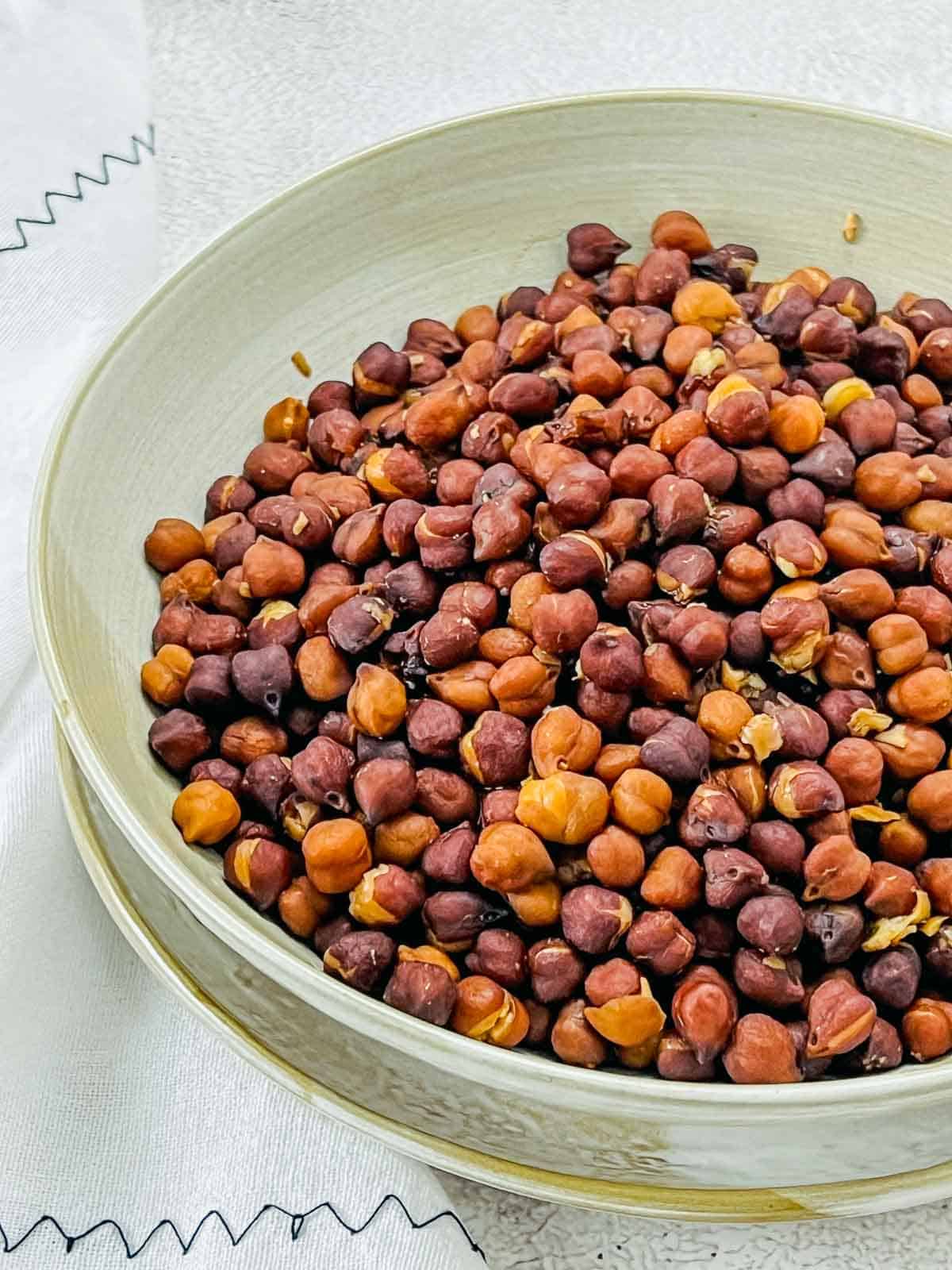 Cooked black chickpeas in a brown bowl on a white surface.