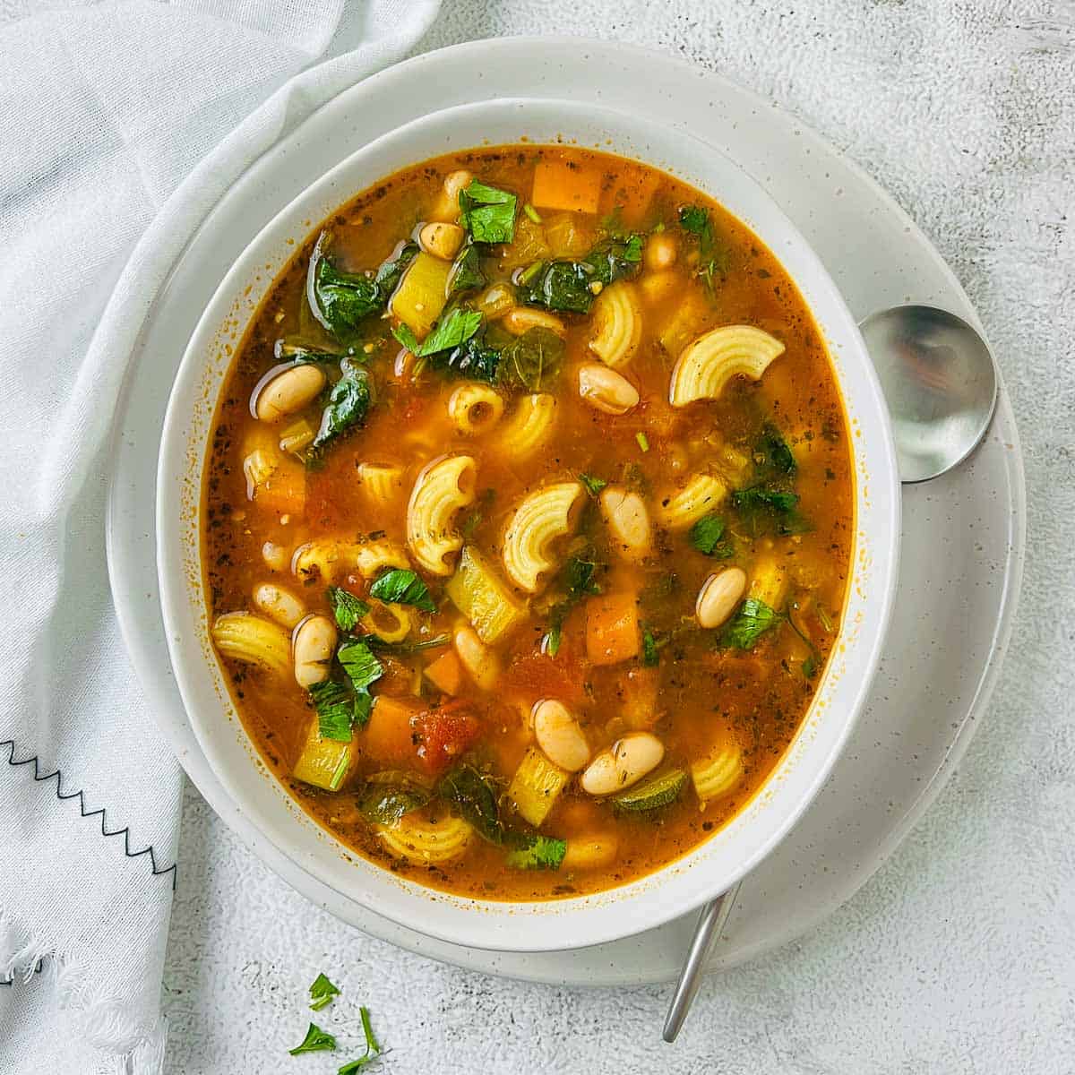 Minestrone soup in a white bowl with a soup spoon in the background.