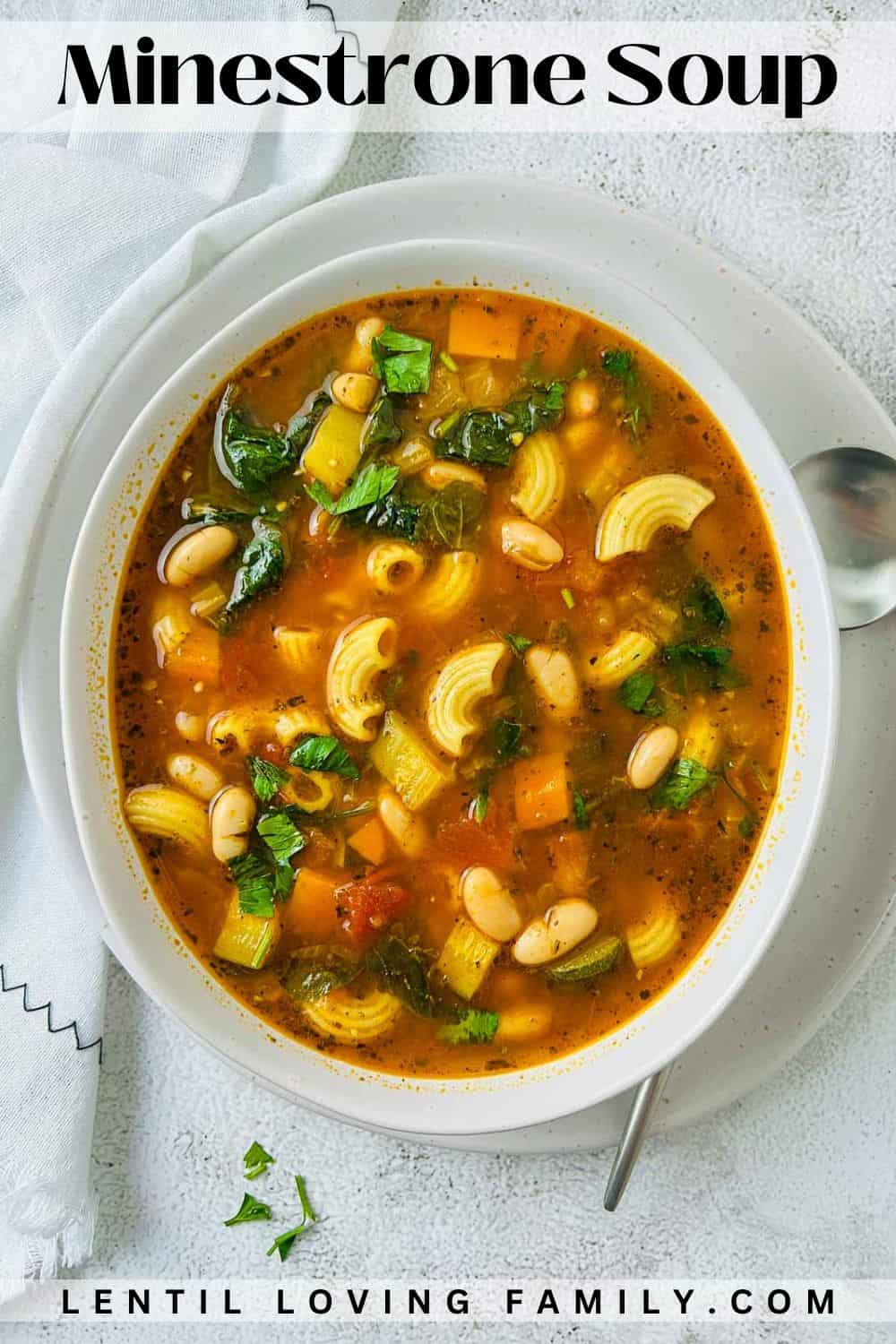 Minestrone soup in a white bowl with spoon in the background.