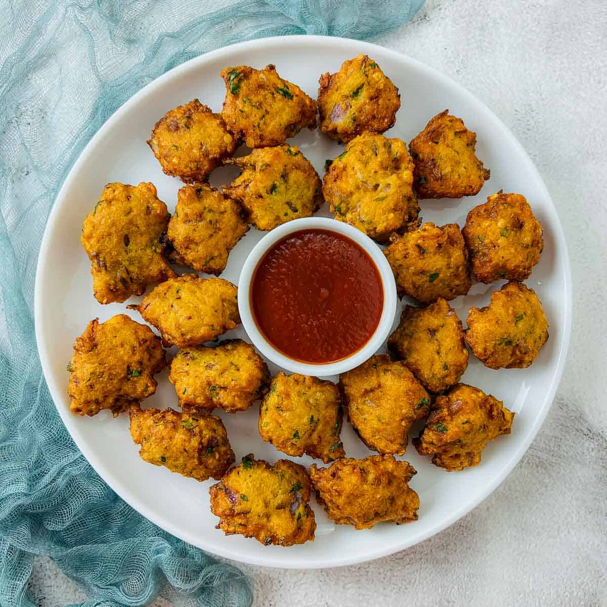 Red lentil fritters on a white plate with ketchup bowl in the center.