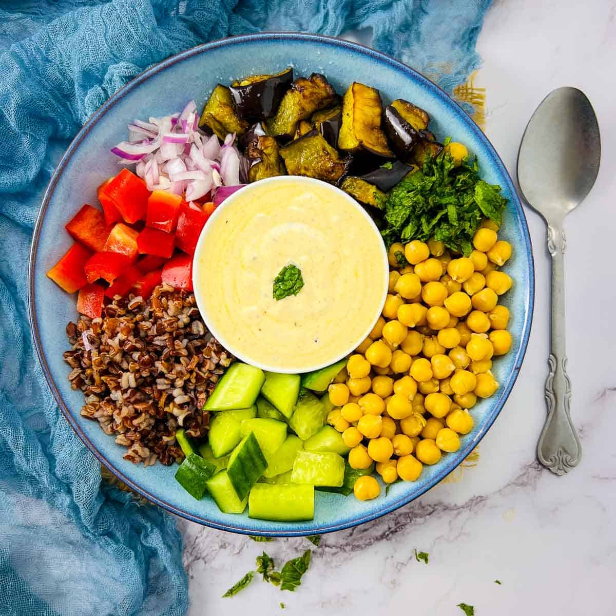 Roasted eggplant and chickpea buddha bowl with yogurt sauce in the center and a spoon in the background.