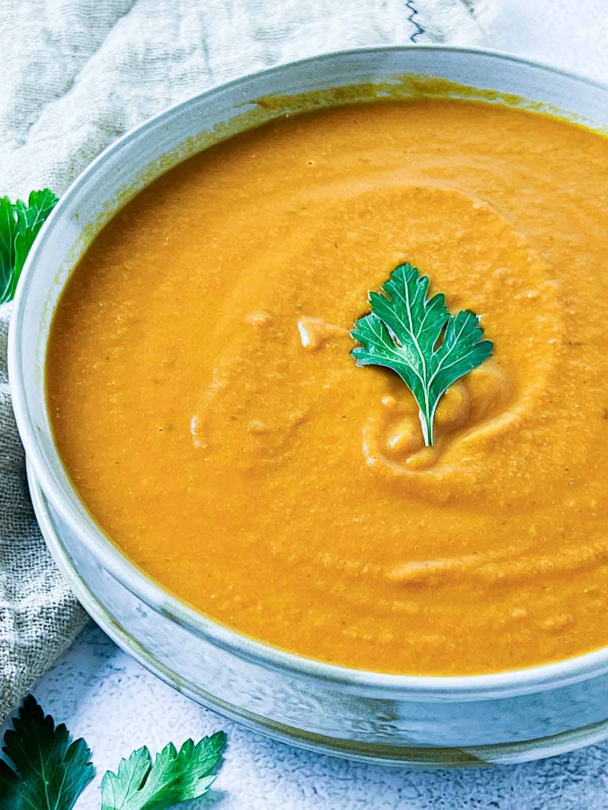 Tomato lentil soup in a brown bowl placed on a browl plate.