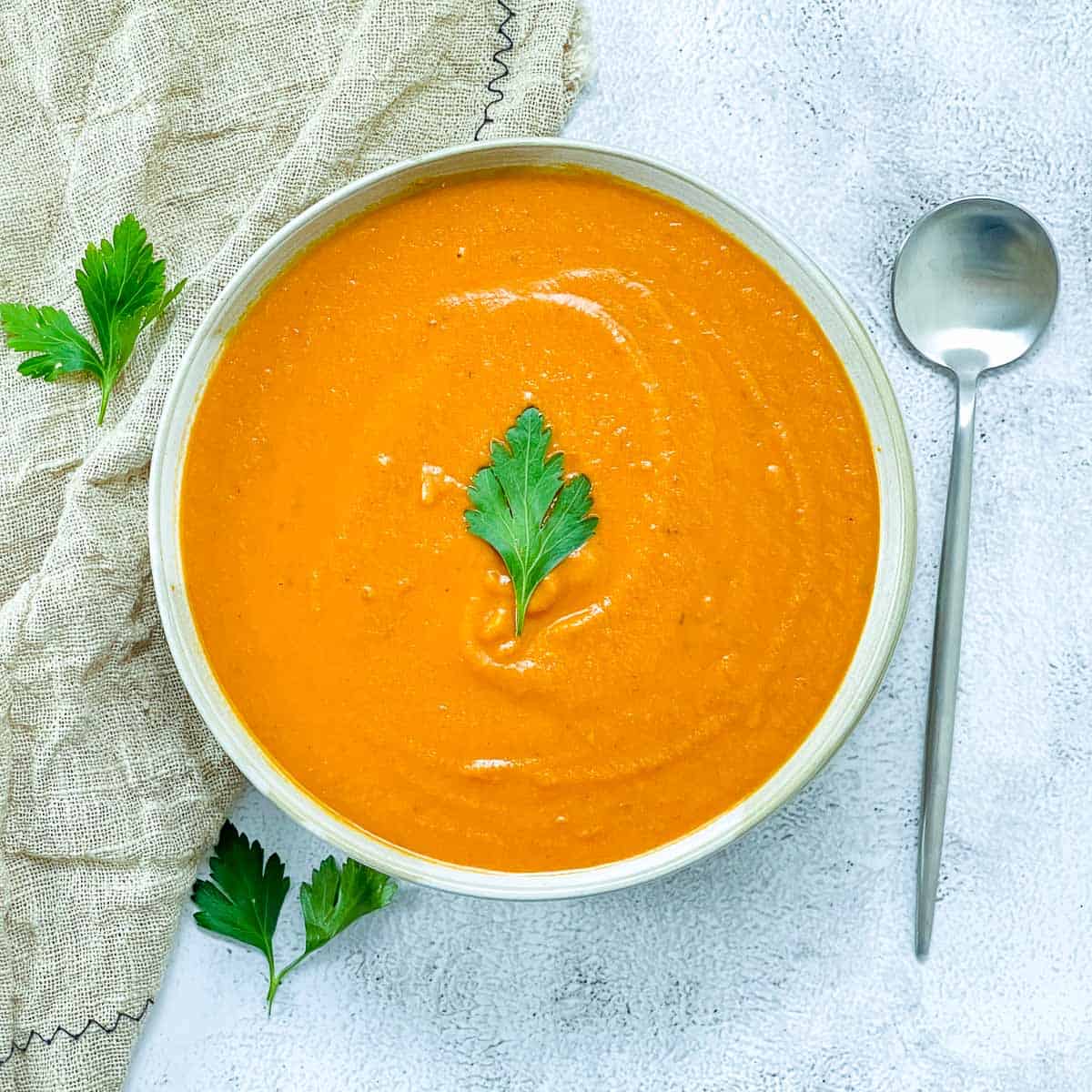 A bowl of tomato lentil soup topped with parsley on a white surface.