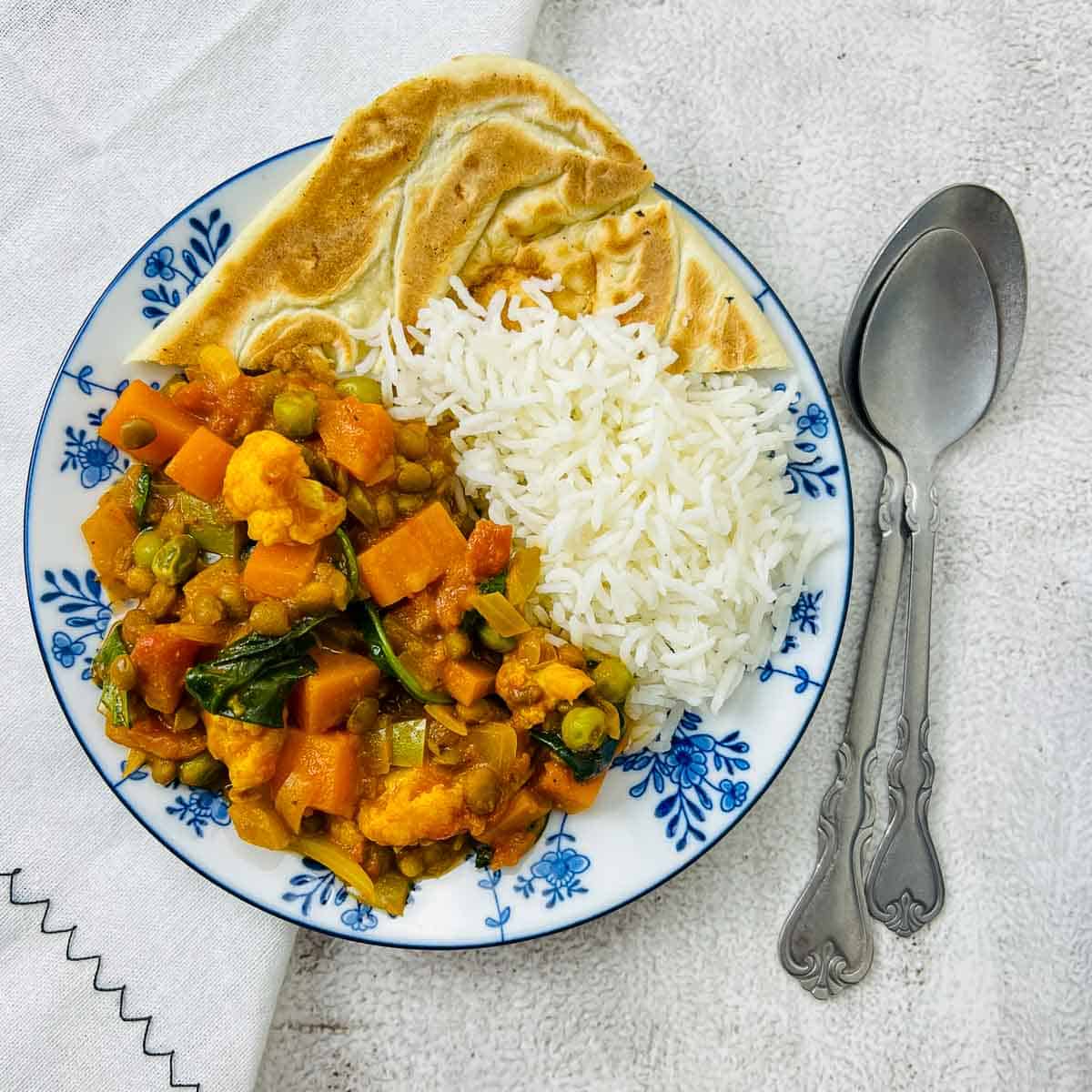 Vegetable lentil curry, rice, and naan bread on a blue plate.