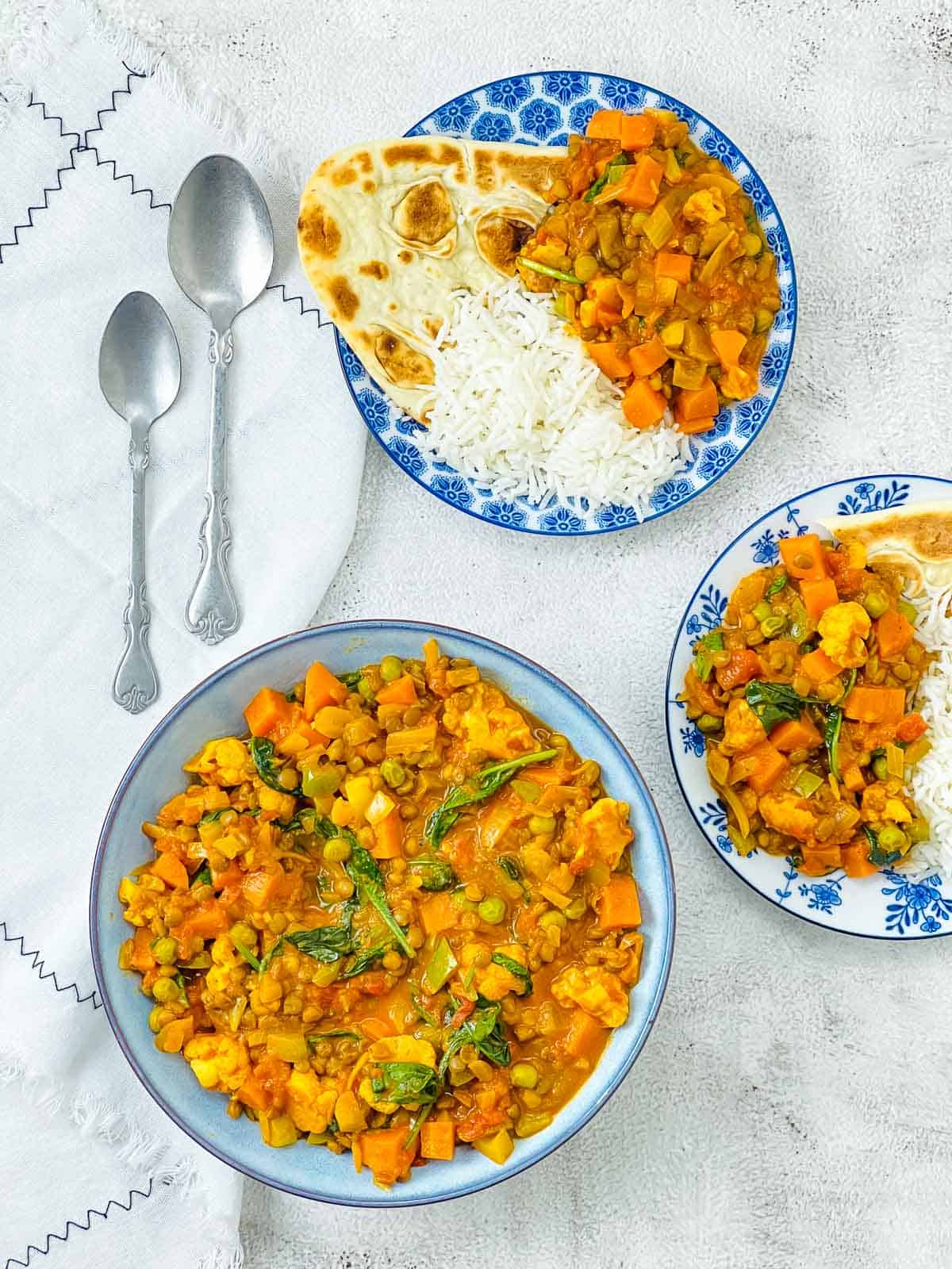 Vegetable lentil curry in blue bowl with rice and naan bread in the background.