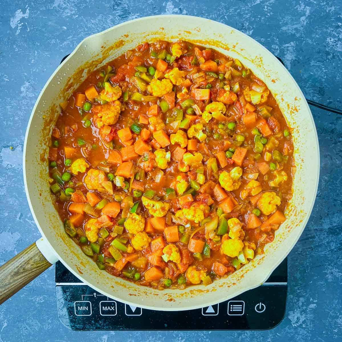 Partially cooked veggies in onion-tomato masala in the frying pan.