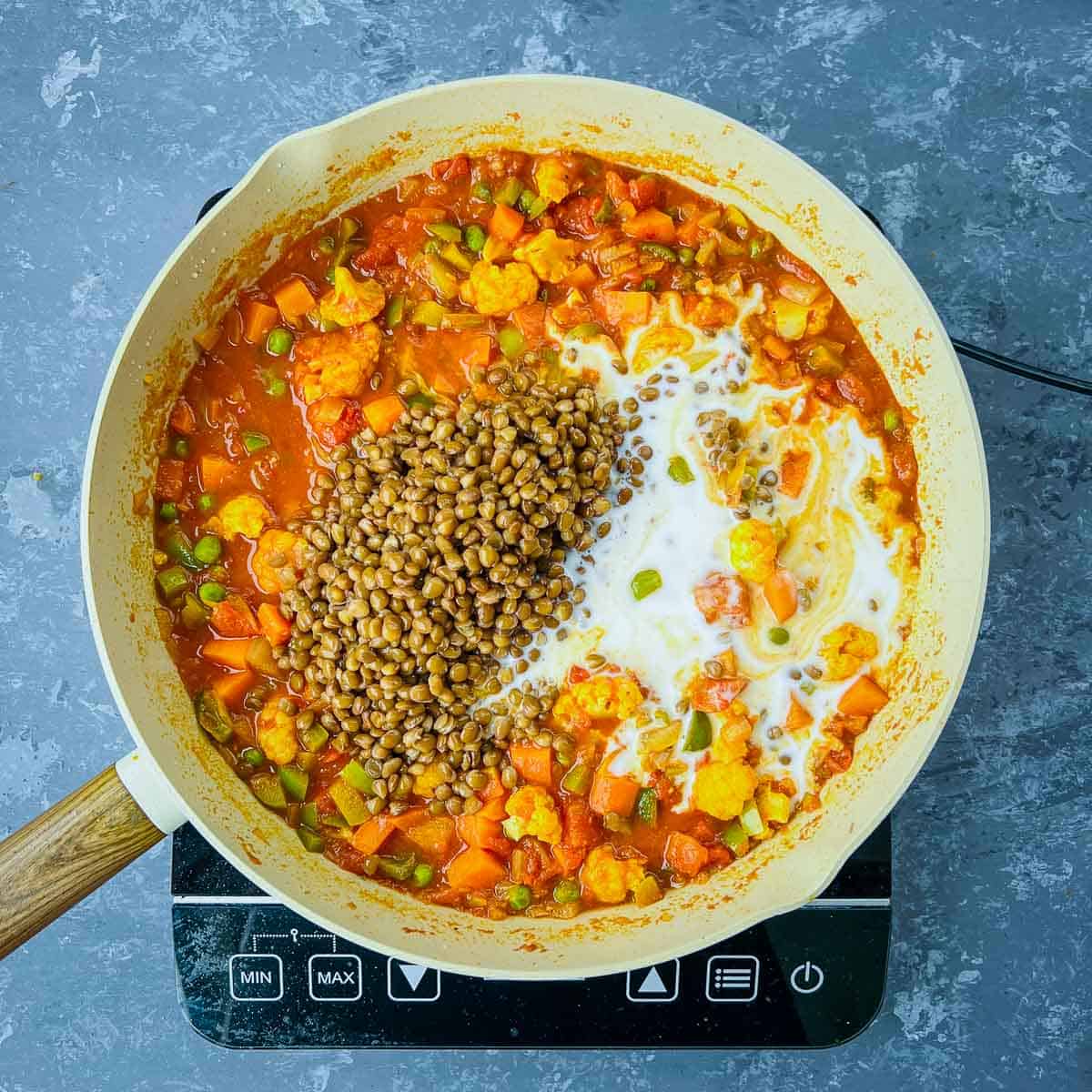 Lentils and coconut milk added to veggies in the frying pan.