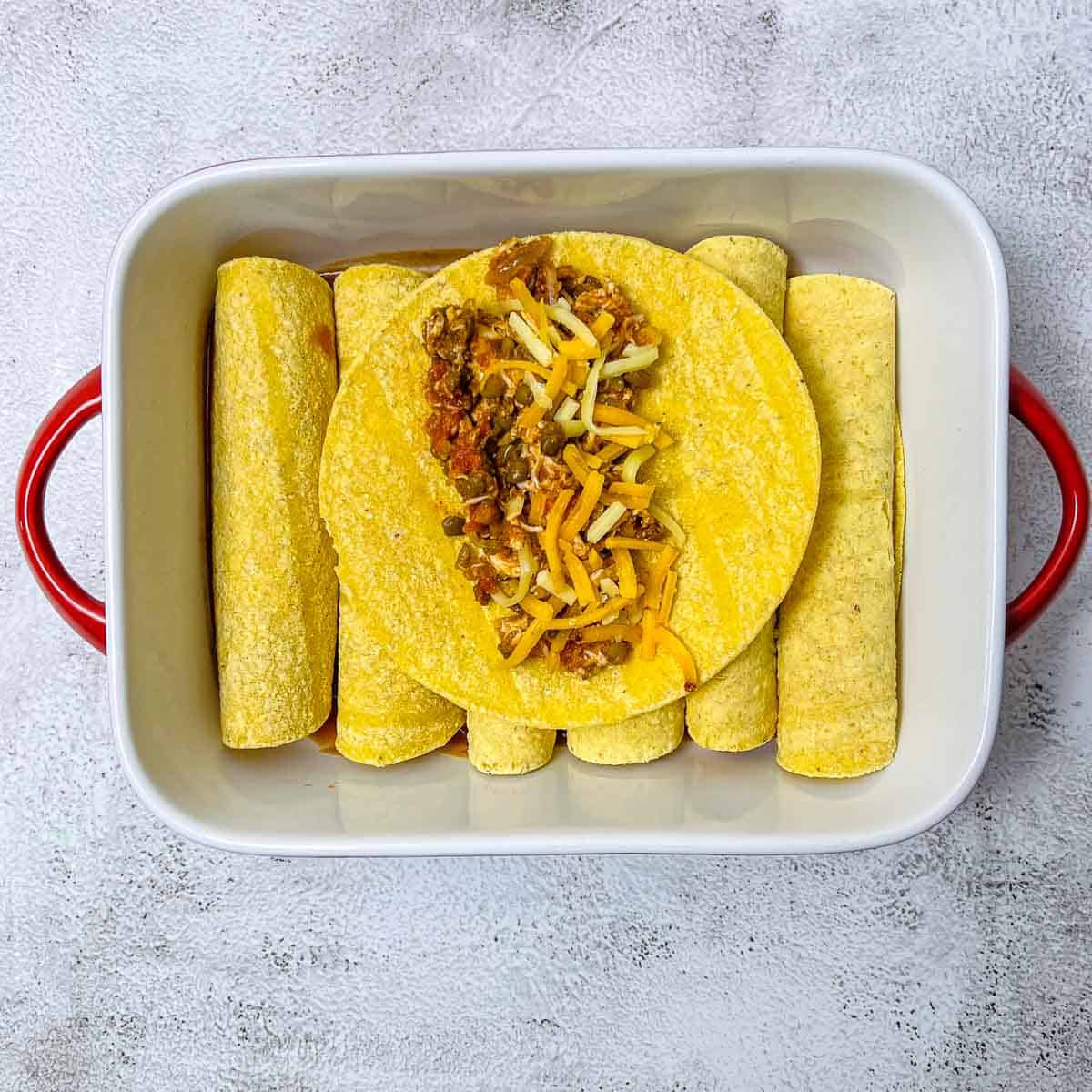 Corn tortilla wraps stuffed with enchiladas filling and cheese.