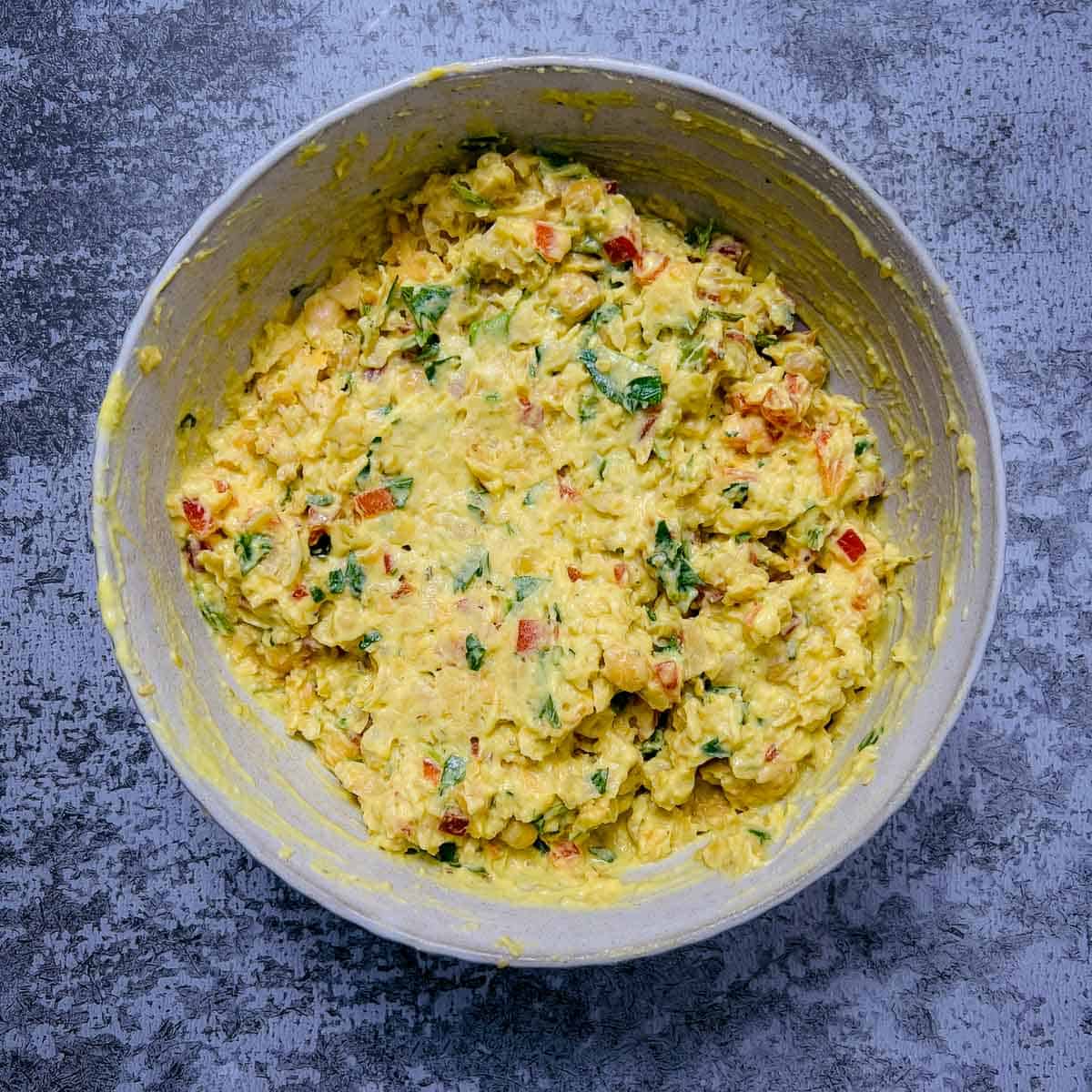 Chickpeas, veggies, and salad dressing mixed together in a white bowl.