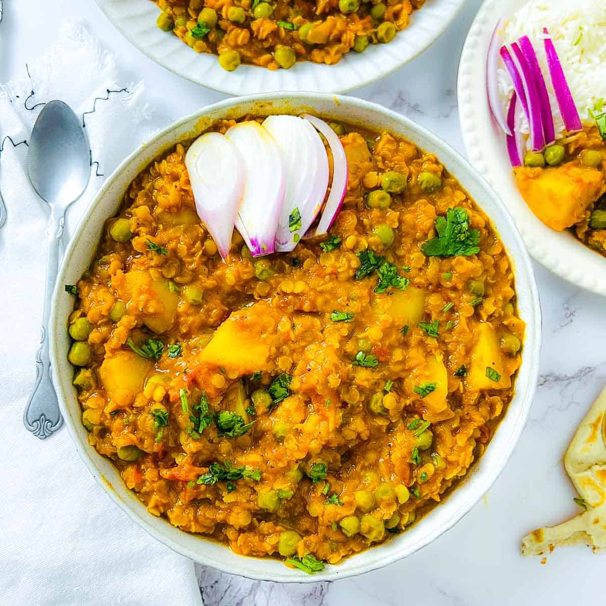 Lentil peas and potato curry in a white bowl garnished with onion slices and cilantro.