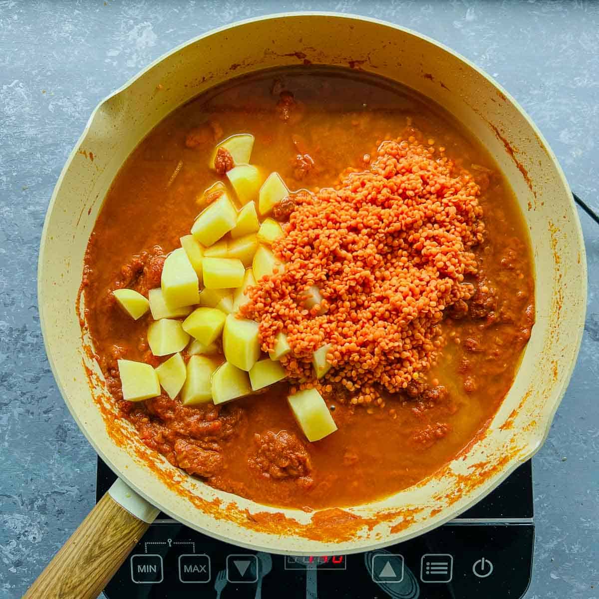 Red lentils, potatoes, and water added to the frying pan.