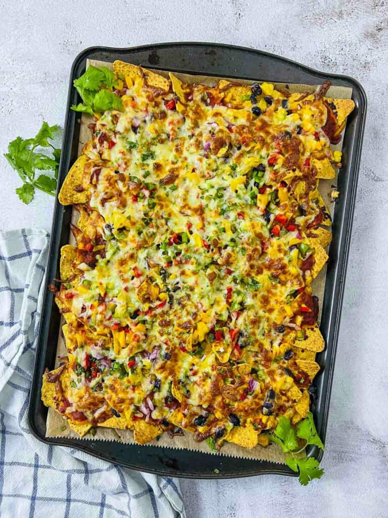 Baked loaded nachos on a white surface with cilantro sprigs in the background.