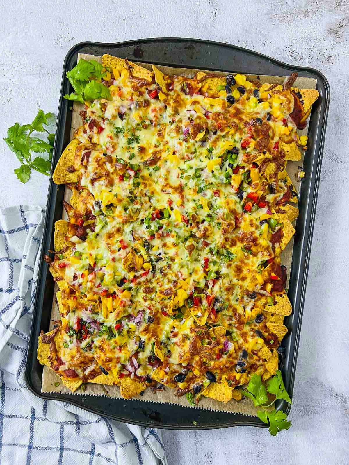 Baked loaded nachos on a white surface with cilantro sprigs in the background.