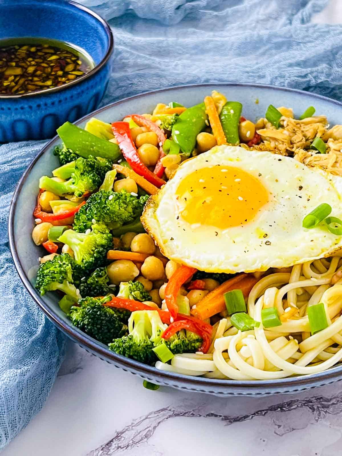 Chicken and chickpea udon noodle bowl topped with a fried egg.