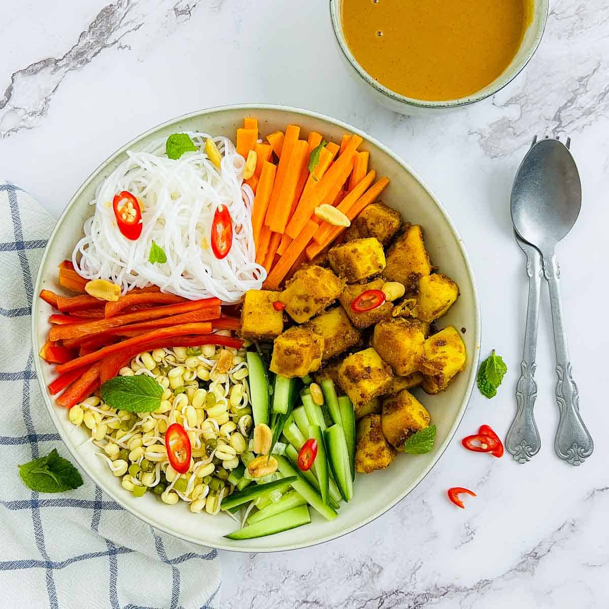 Chickpea tofu Buddha bowl garnished with sliced red chilies on a marble surface.