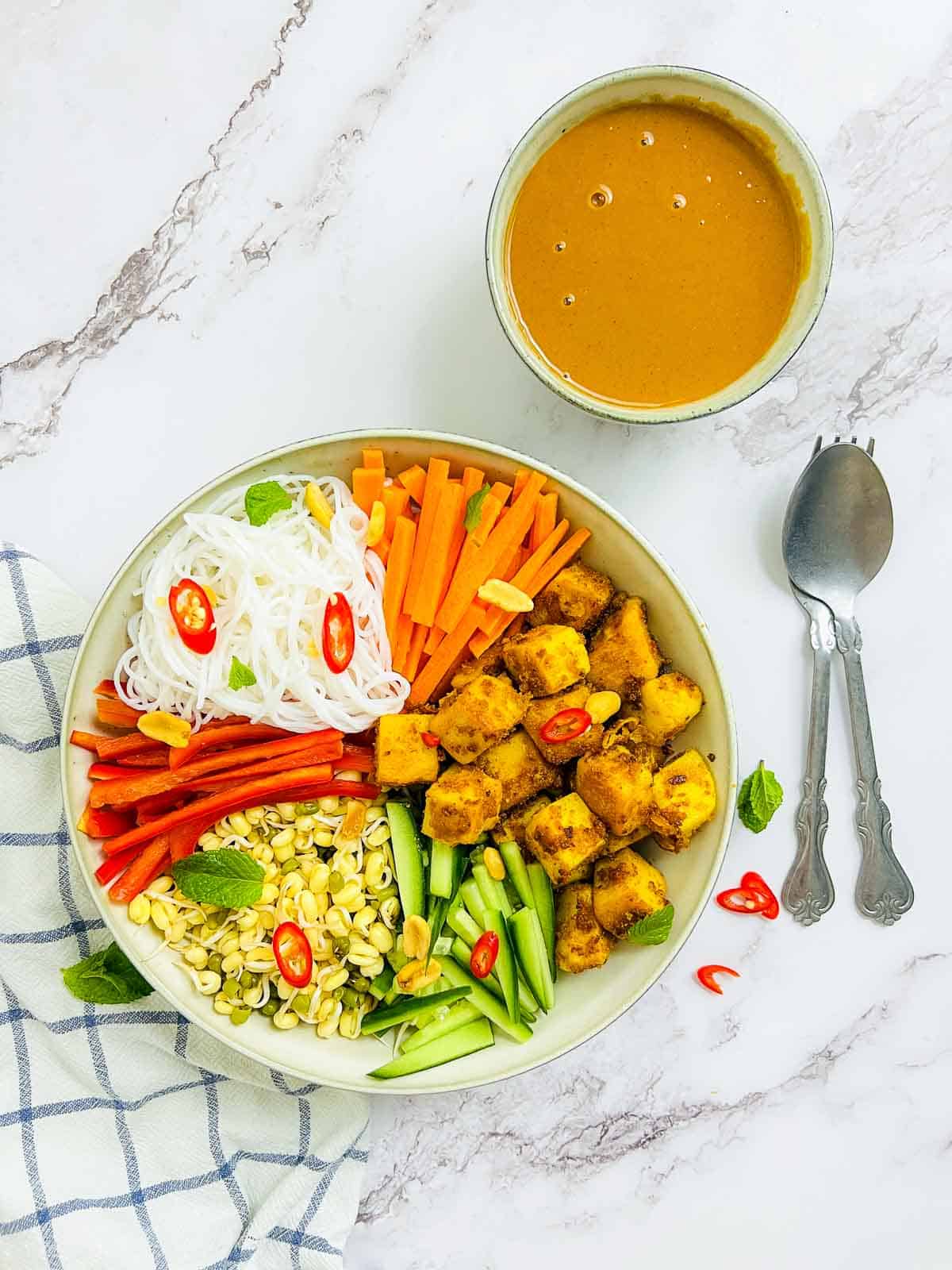 Chickpea noodle Buddha bowl on a white surface with spoon in the background.