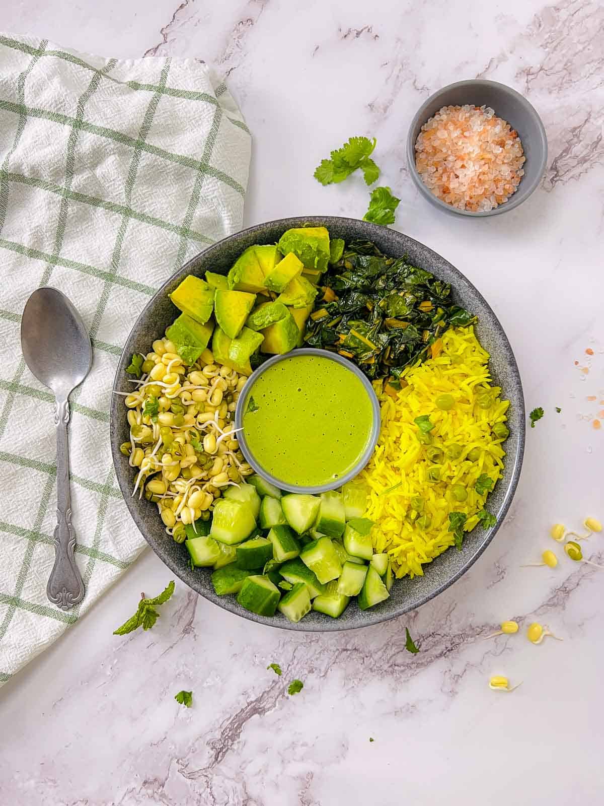 Green goddess power bowl on a white surface with spoon and a bowl of salt in the background.