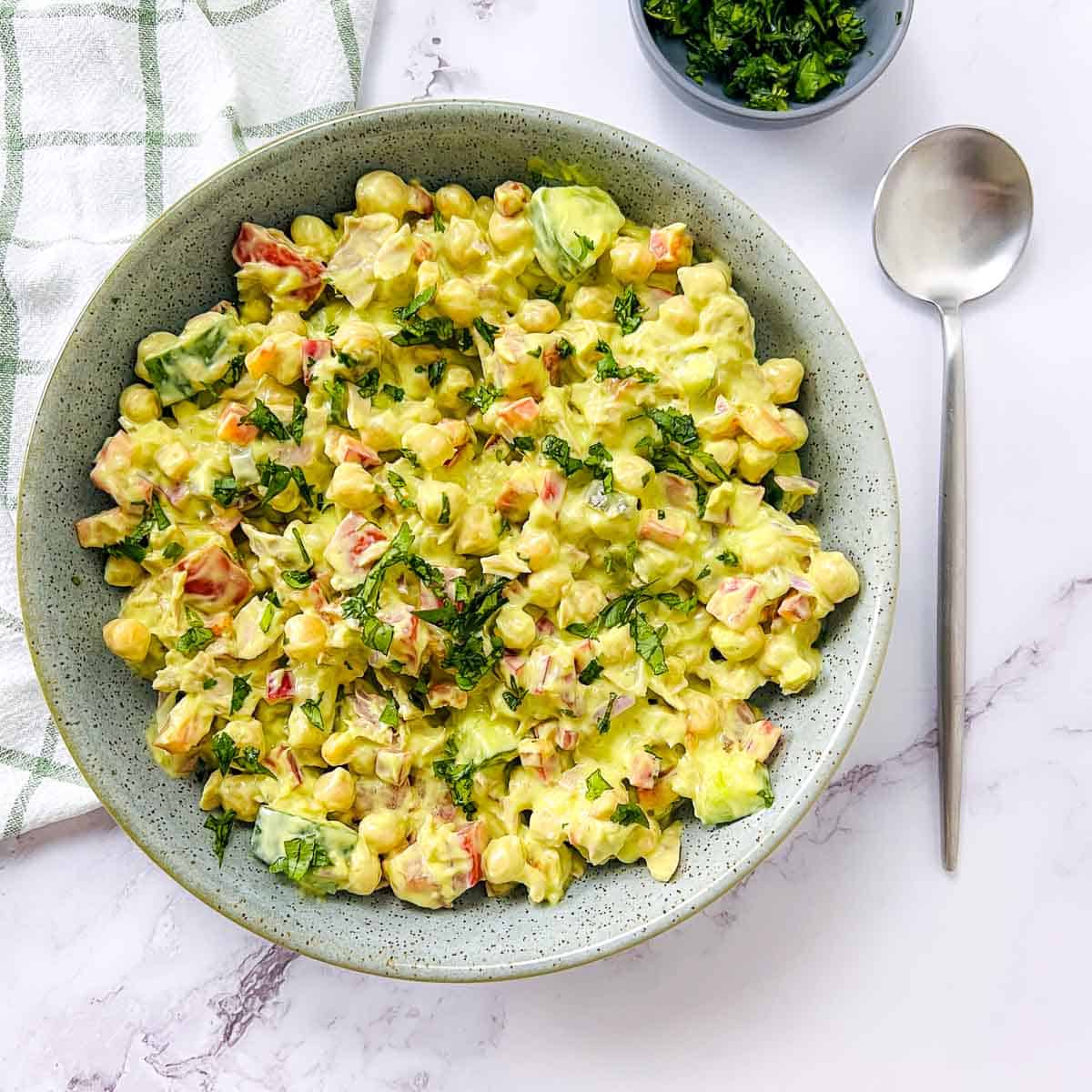 Tuna chickpea salad with avocado dressing in a green bowl with a spoon on the side.
