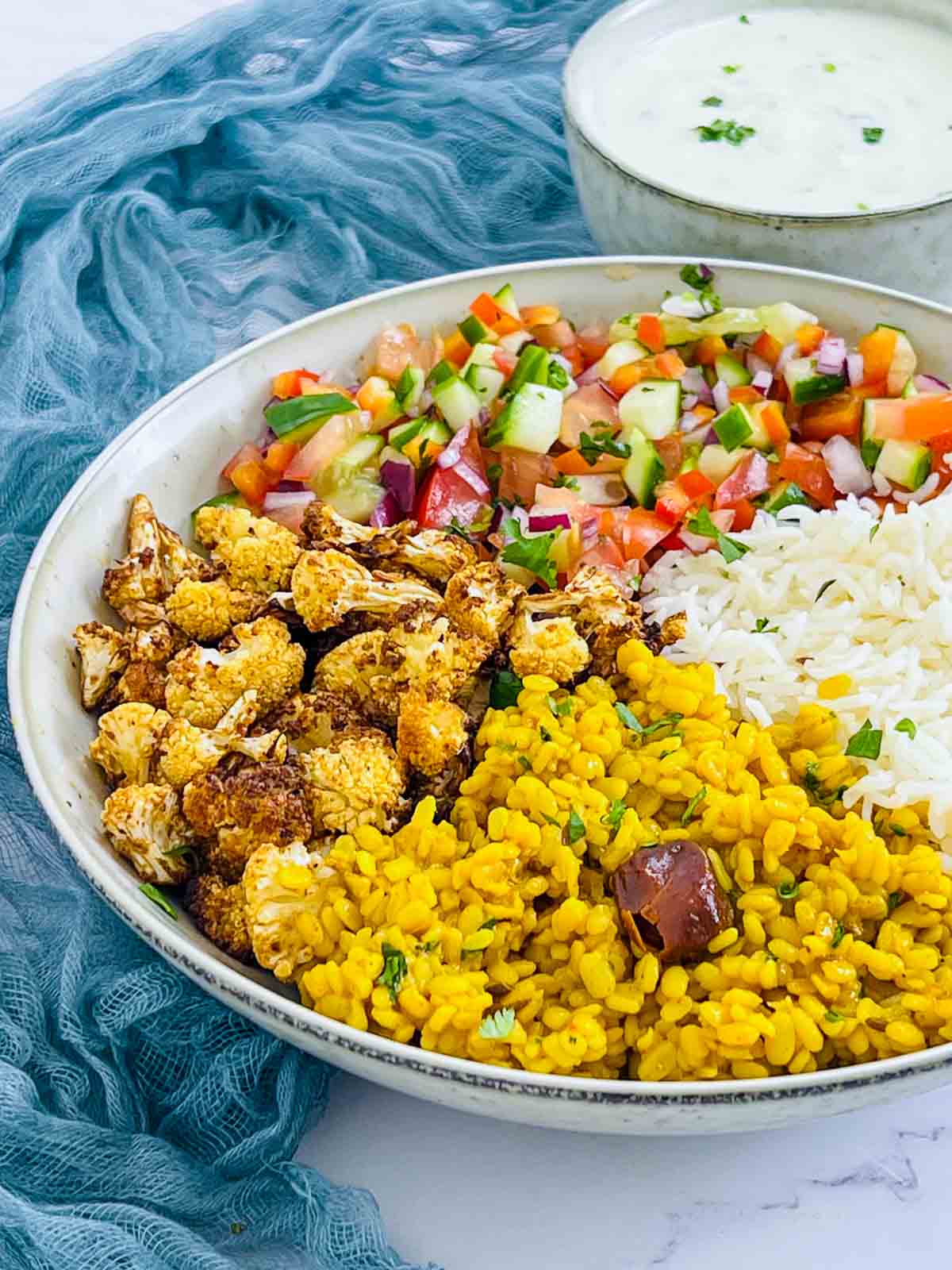 Yellow lentil Buddha bowl on a white surface with raita bowl in the background.