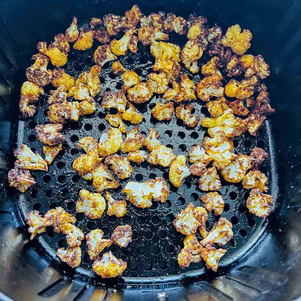 Roasted cauliflower in air fryer basket.
