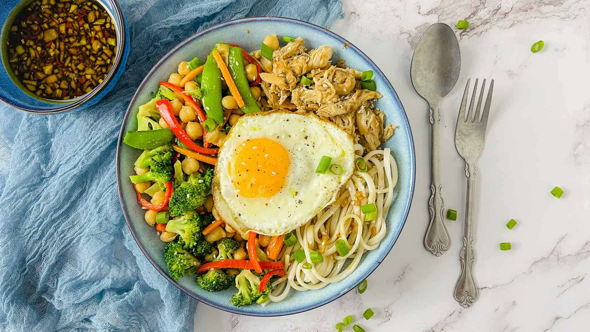 Chicken and chickpea udon noodle bowl on a white surface.