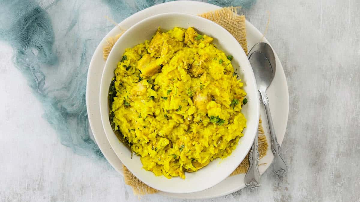 Chicken khichdi in a white bowl with spoons in the background.
