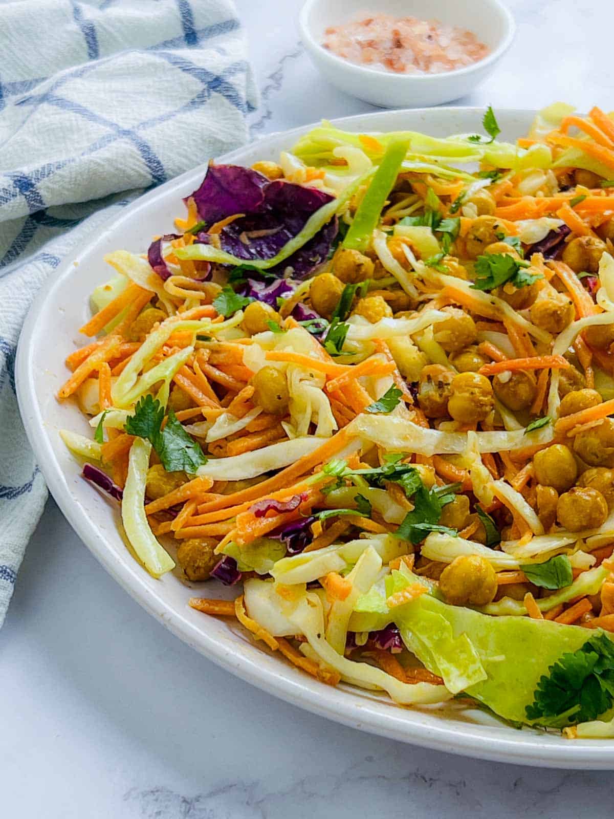 Roasted chickpea crunch salad on a white plate with sea salt in the background.
