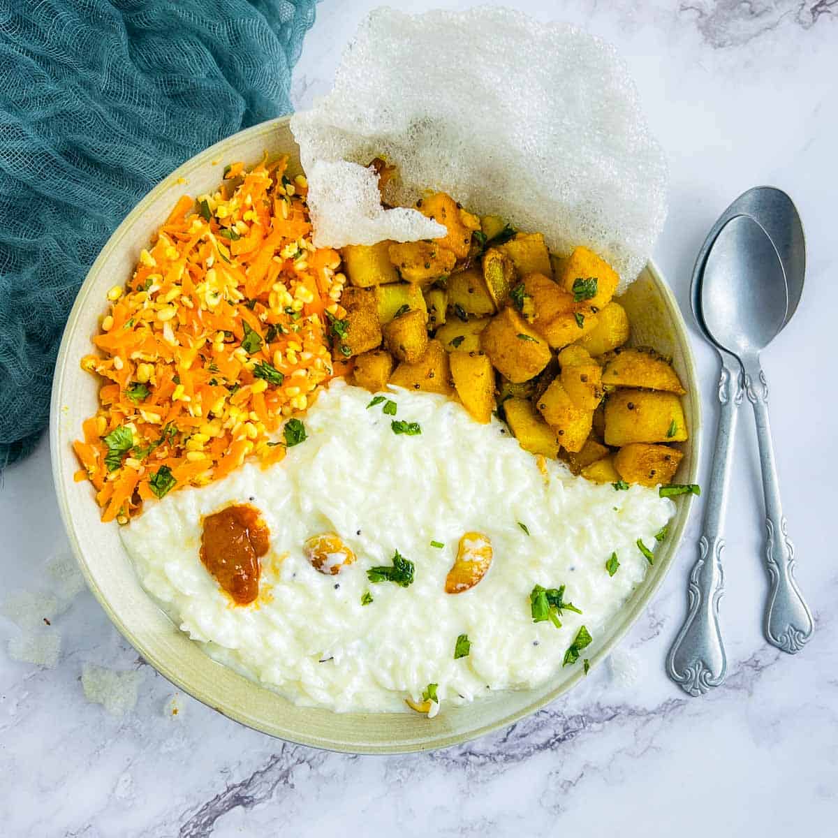 Curd rice bowl on a white surface with spoons in the background.