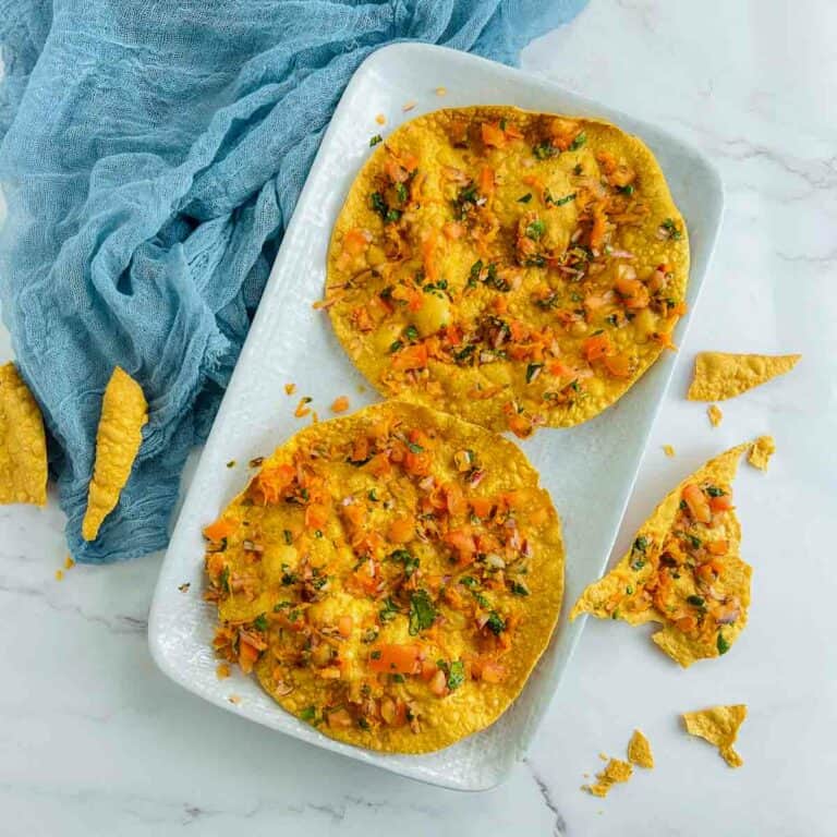 Masala papad on a serving plate with crushed papad pieces on the surface.