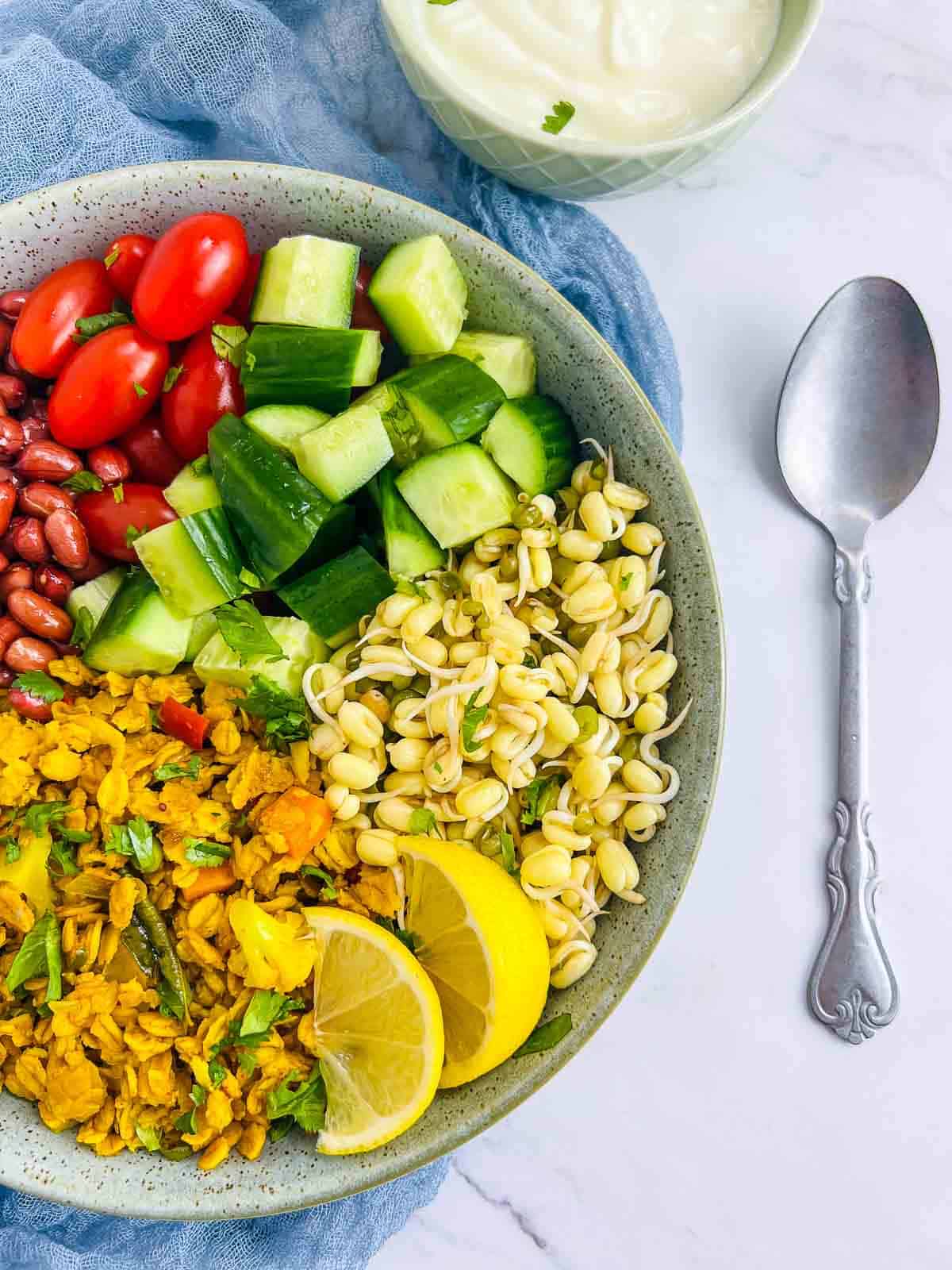 Oats upma assembled with fried peanuts, veggies, and sprouts, with yogurt bowl in the background.