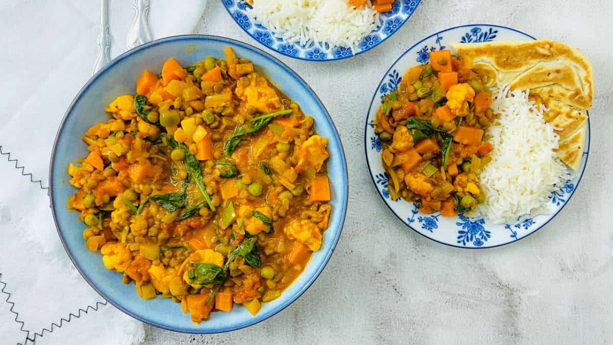 Brown lentil curry in a blue bowl served with naan and rice.