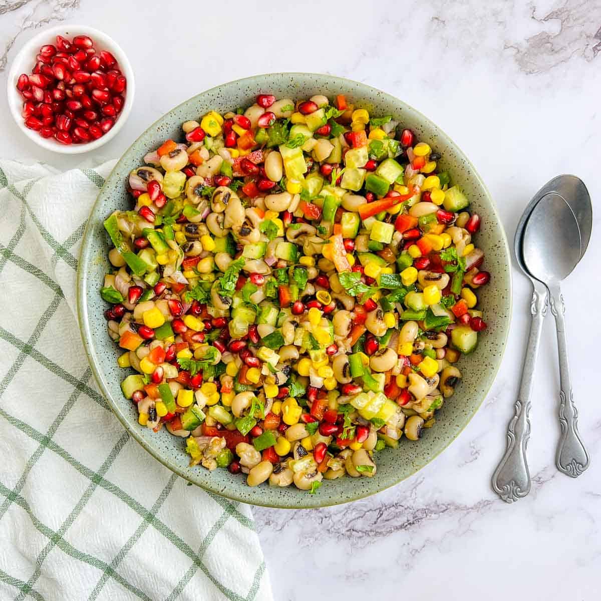 Black-eyed peas salad in a green bowl with spoons in the background.