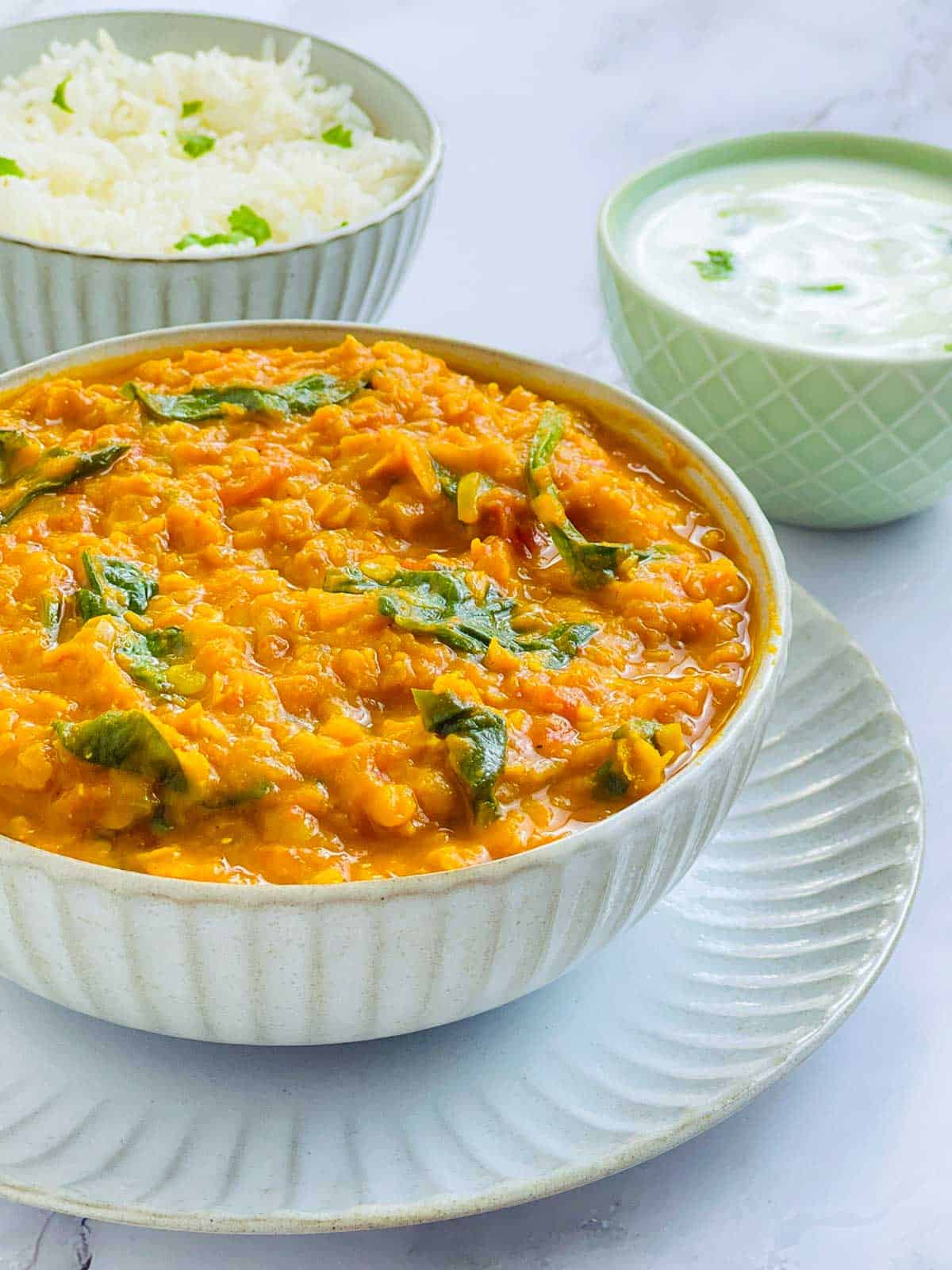 A bowl of red lentil dal placed on a white plate.