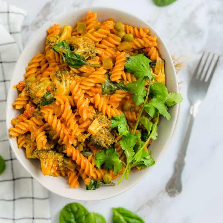 Red lentil pasta on a marble surface with spinach leaves in the background.
