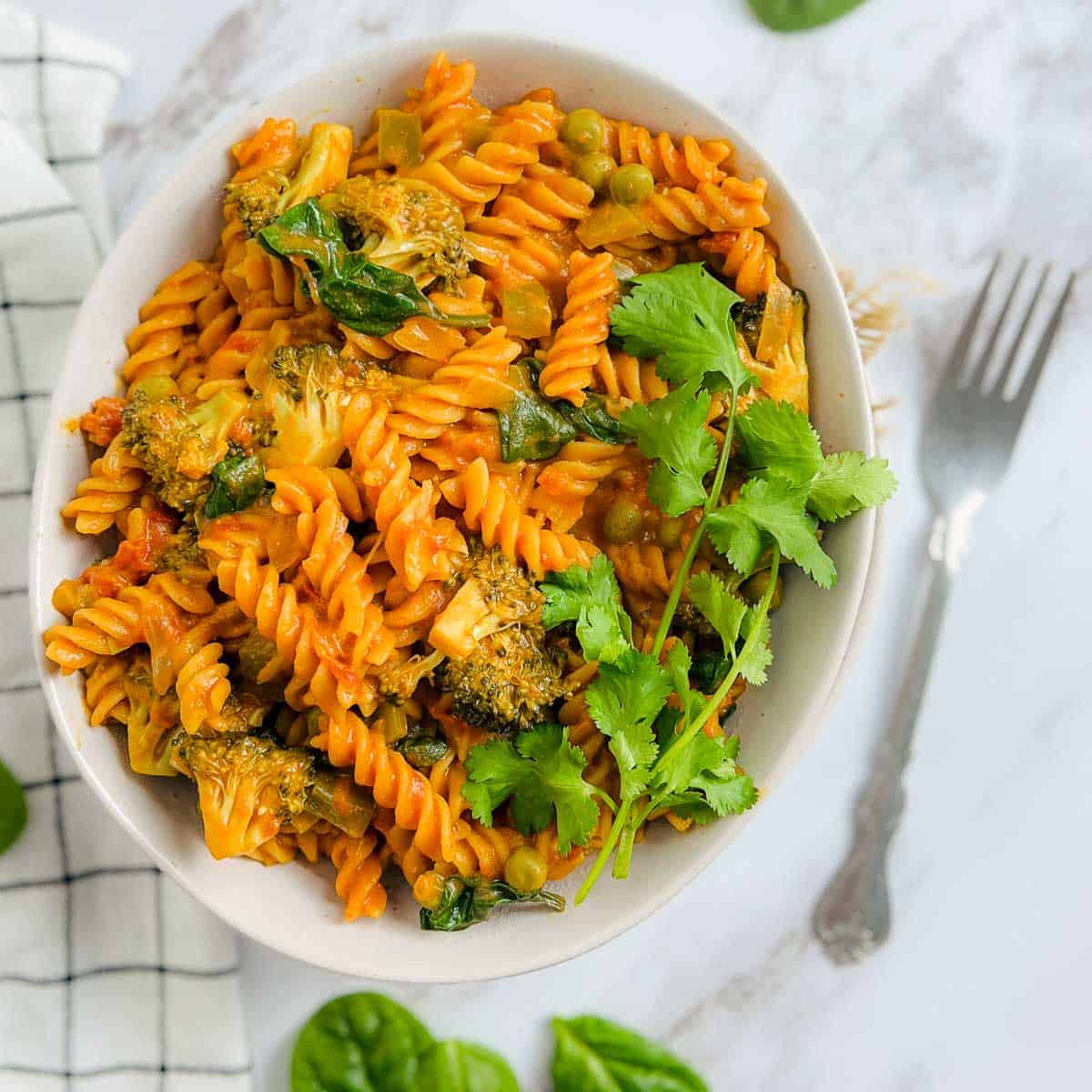 Red lentil pasta on a marble surface with spinach leaves in the background.