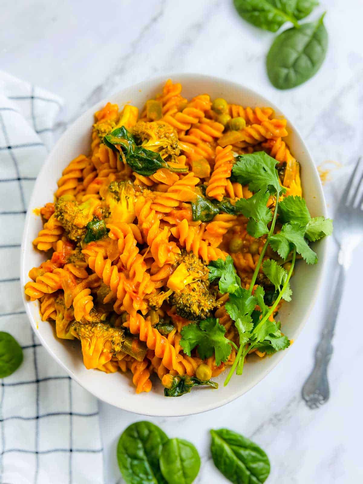 A white bowl full of red lentil pasta with a fork in the background.