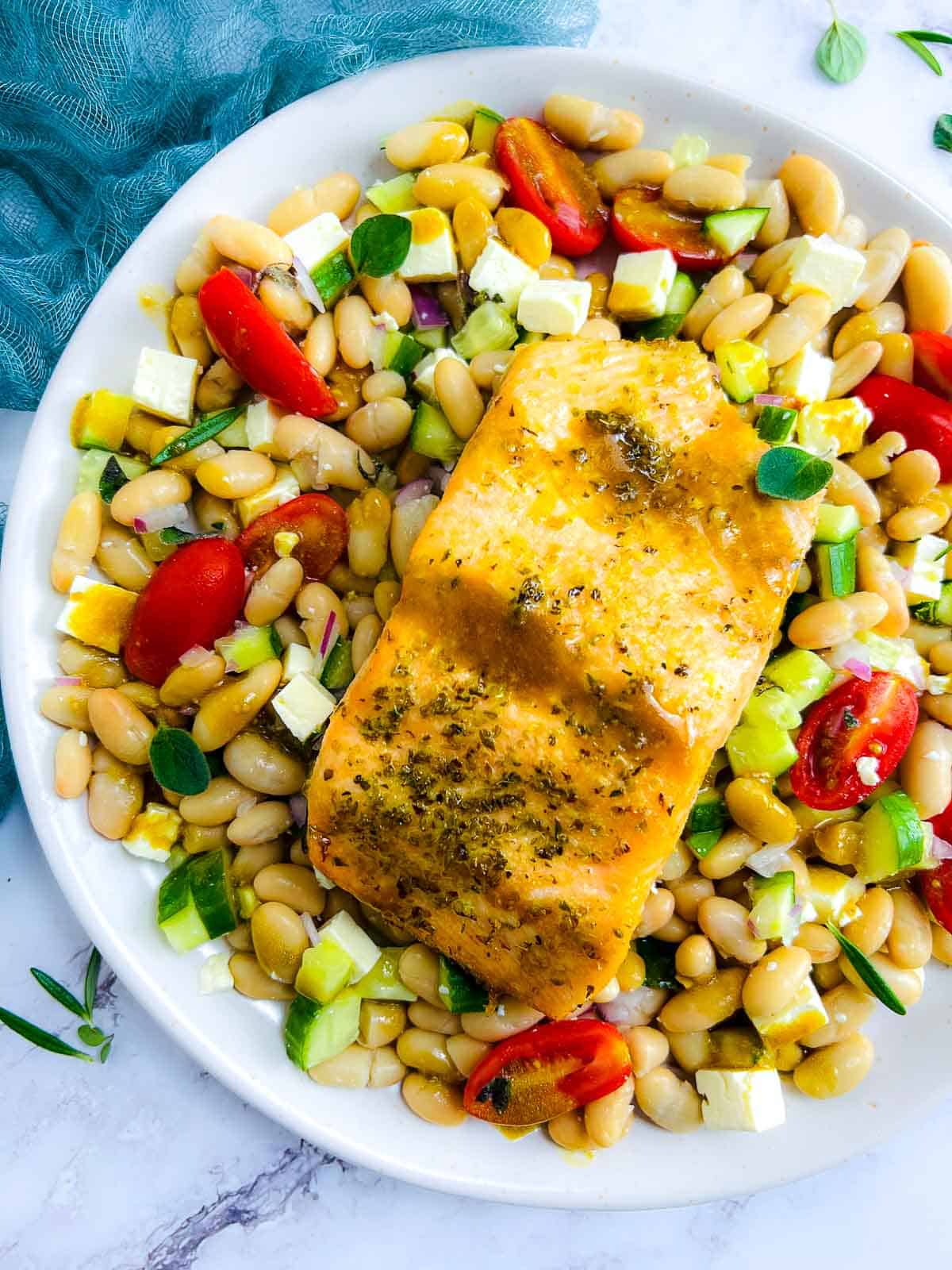 Salmon and bean salad on a white plate with dressing drizzled on the top.