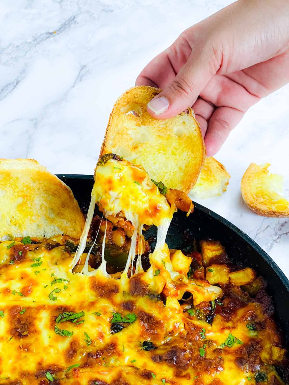Crusty bread dipping into the cheesy tomato bake.