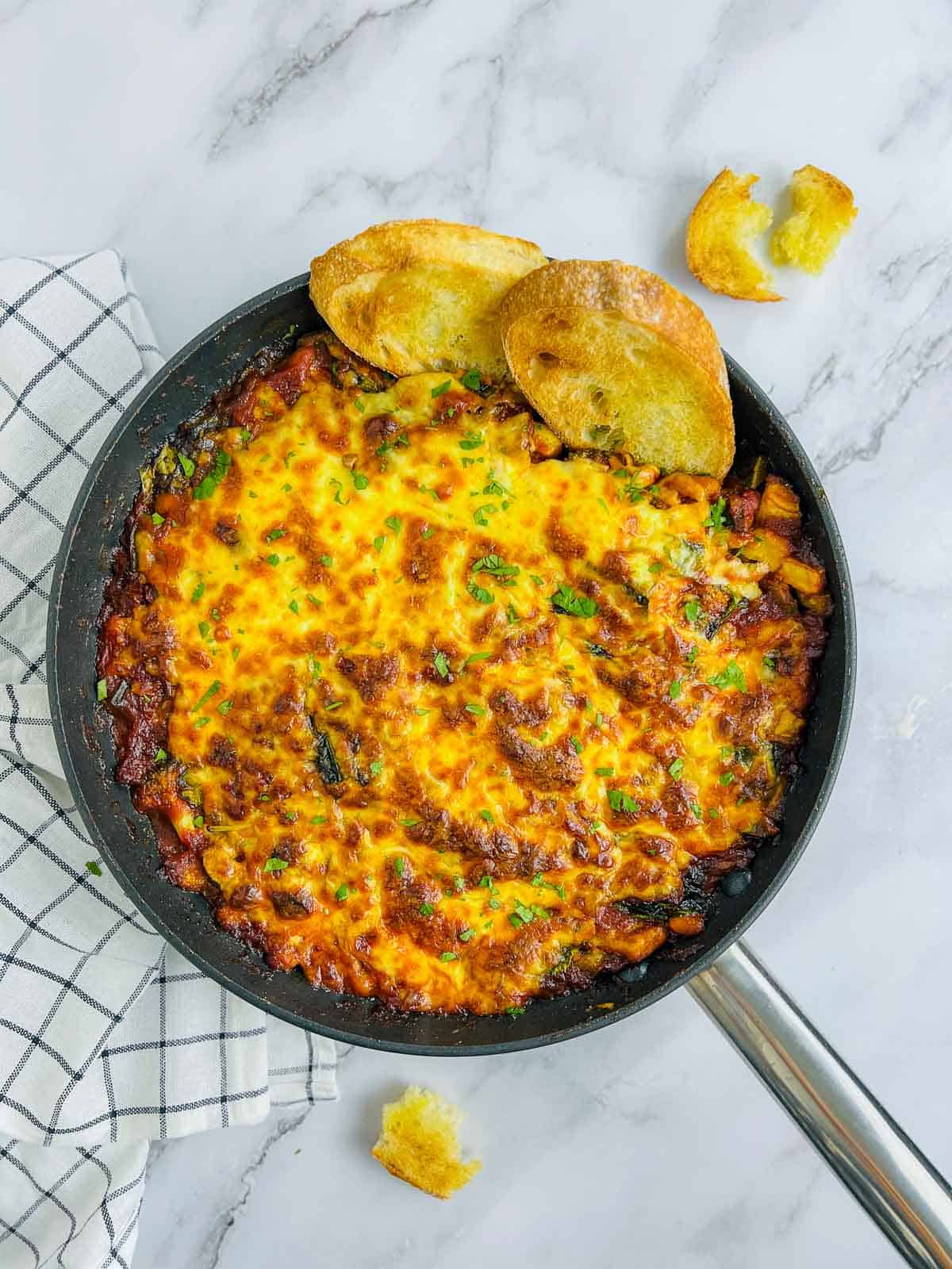 White bean and tomato bake skillet on a marble surface with a check cloth in the background.