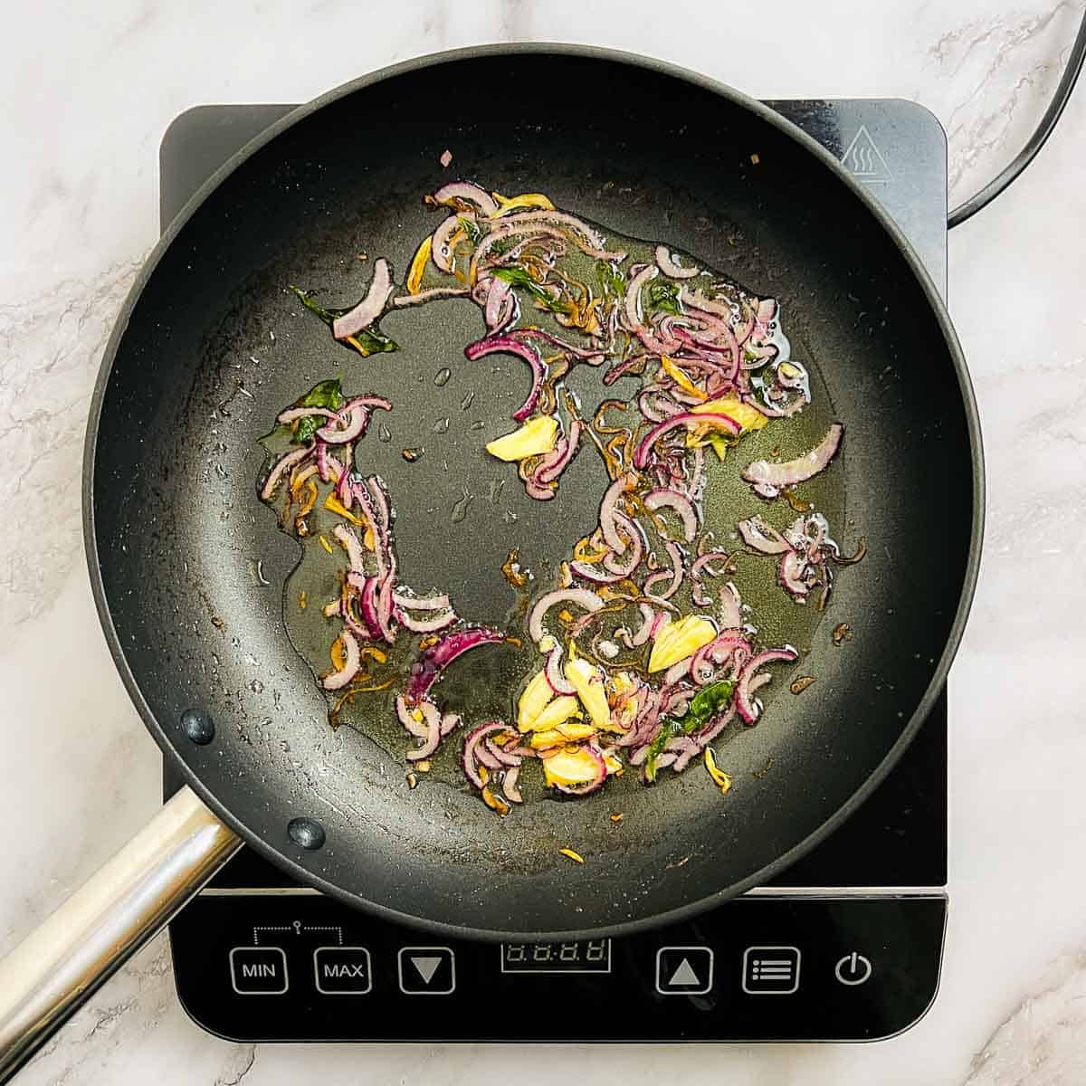 Sauted onion, garlic, and curry leaves in a frying pan.